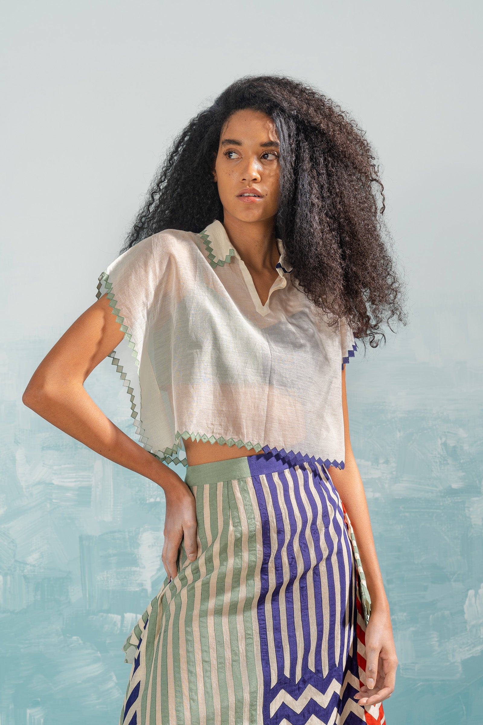 Woman wearing a white blouse with lace details and a colorful skirt against a light blue background