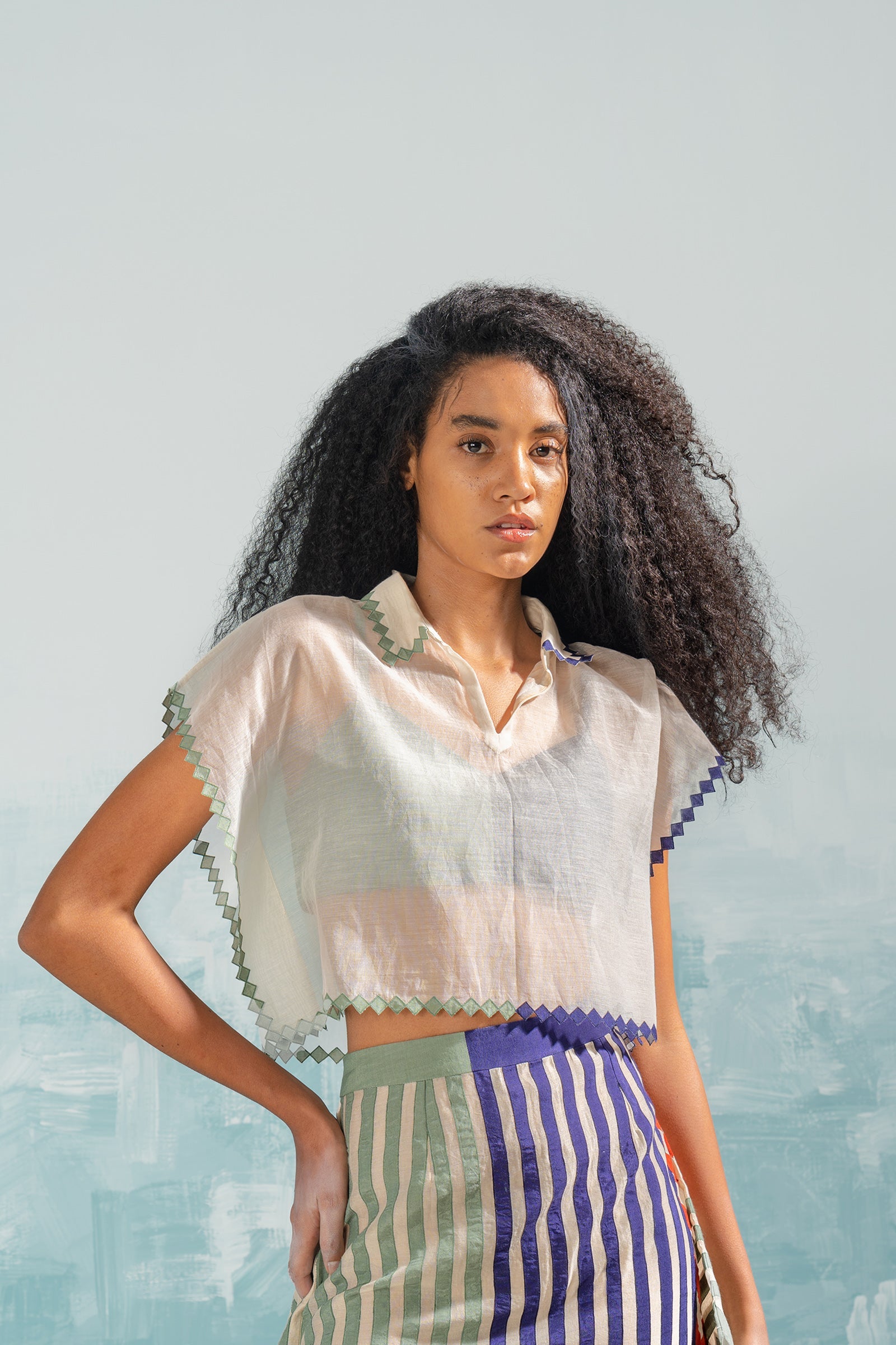 Woman wearing a white blouse with ruffled sleeves and a striped skirt against a light blue background