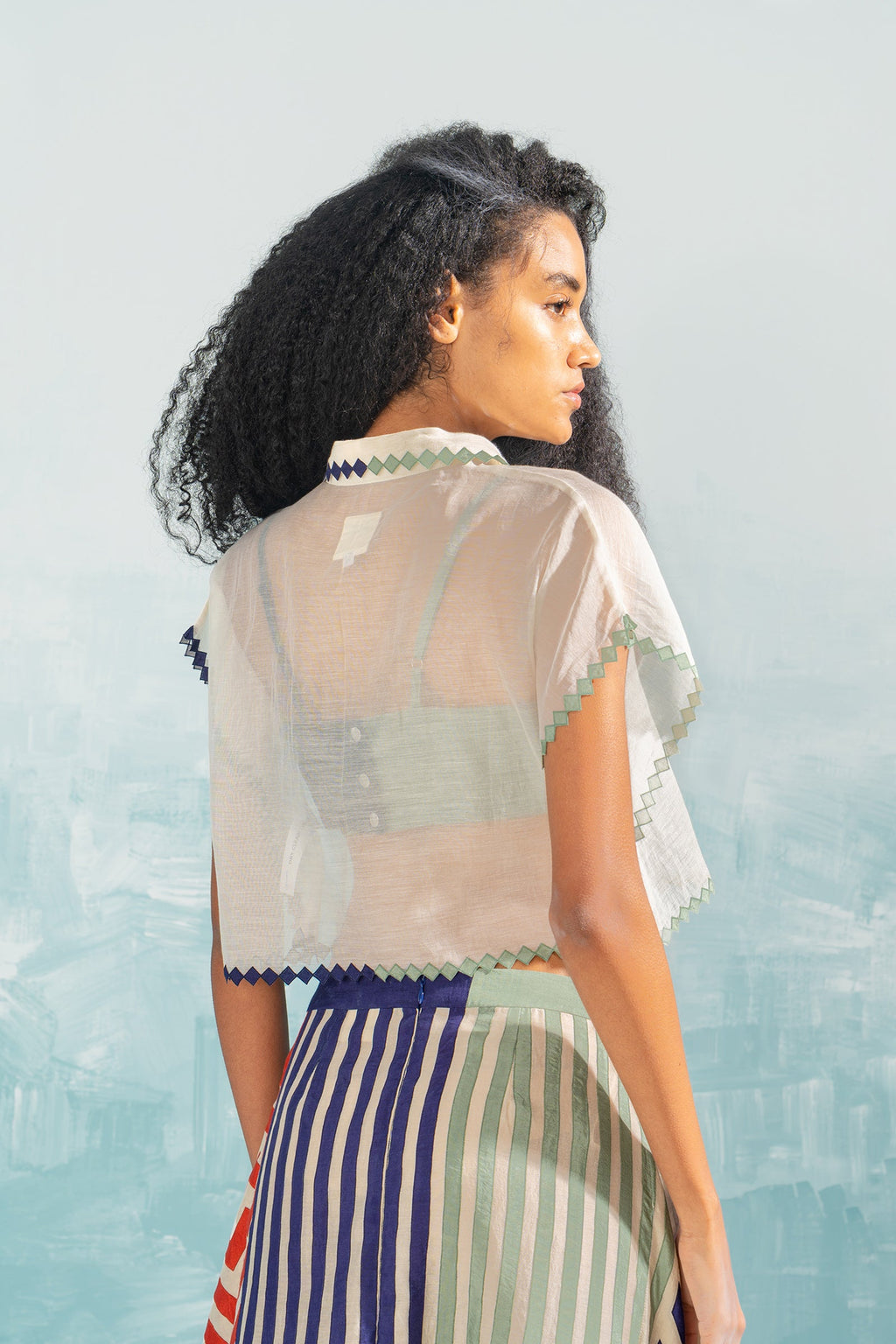 Woman wearing a sheer top with a striped skirt against a light blue background