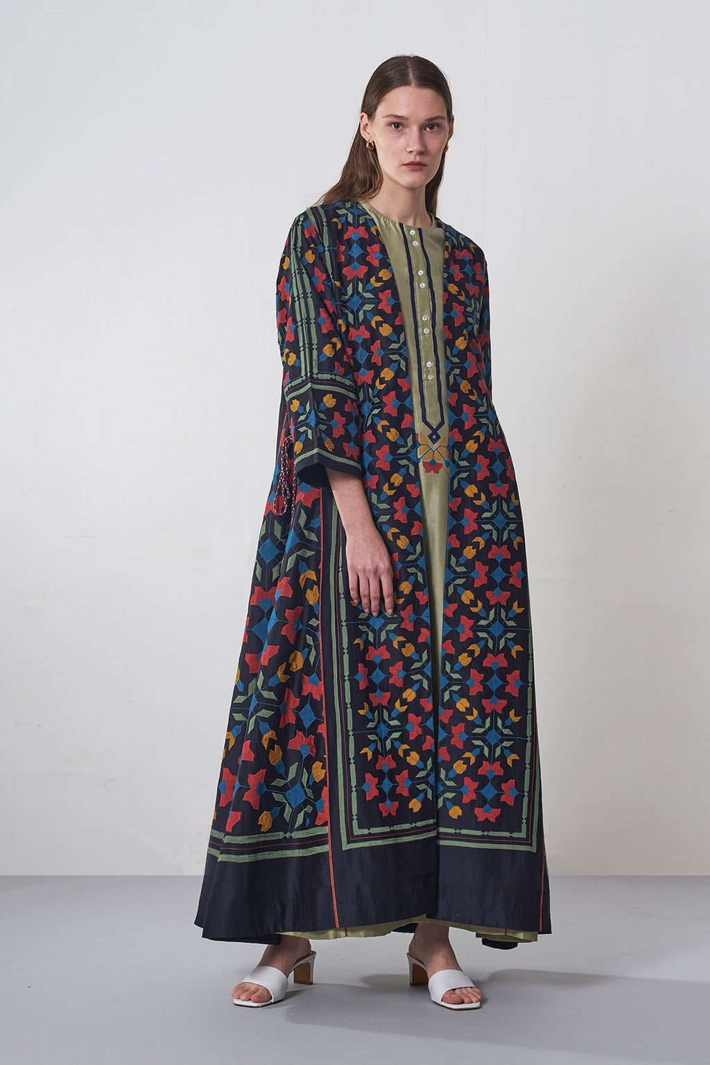 Beautiful Woman wearing a long, patterned embroidered fashion luxury dress jacket against a white background