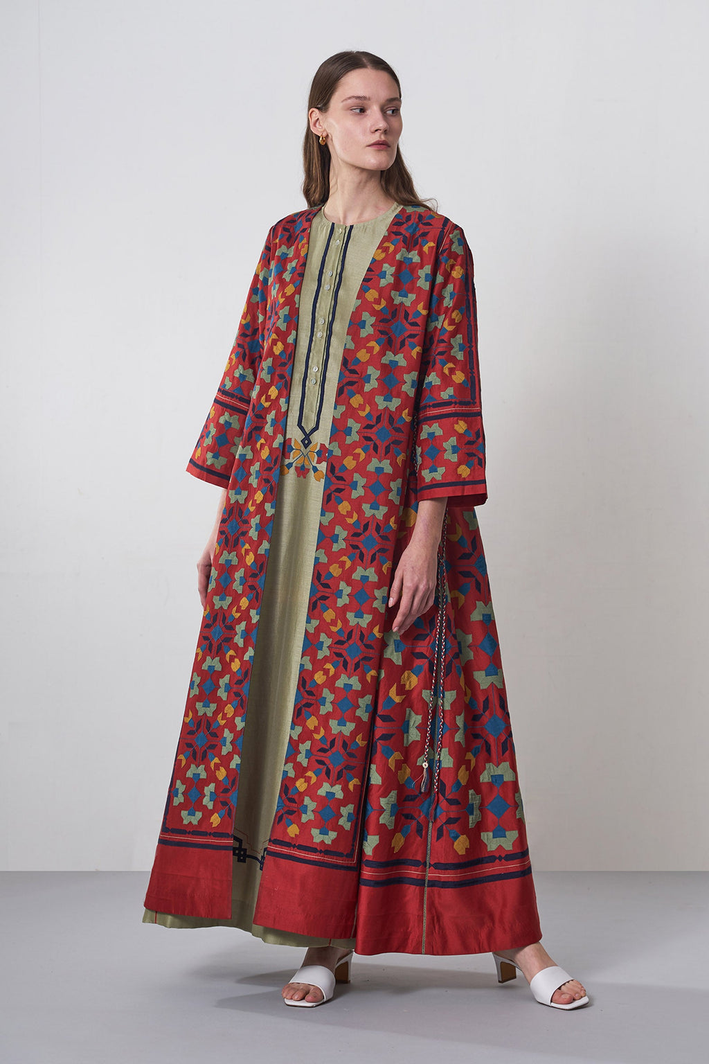 Woman wearing a long, patterned dress with a colorful floral design on a plain background