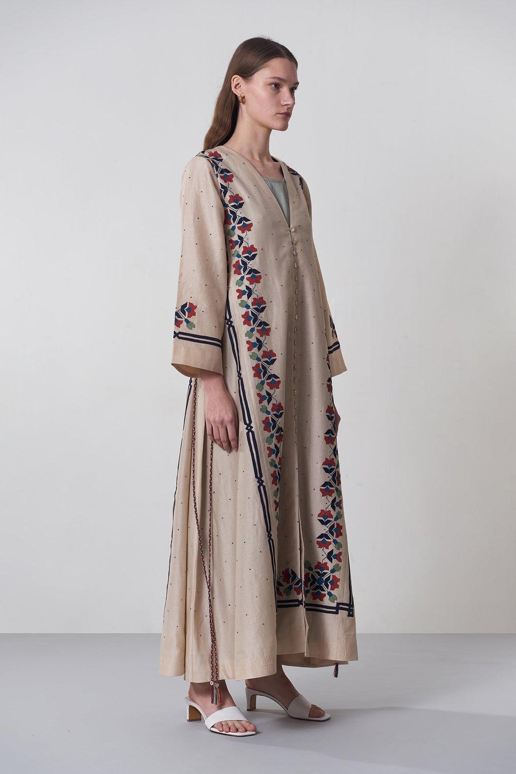 Woman wearing a long, embroidered dress on a plain background