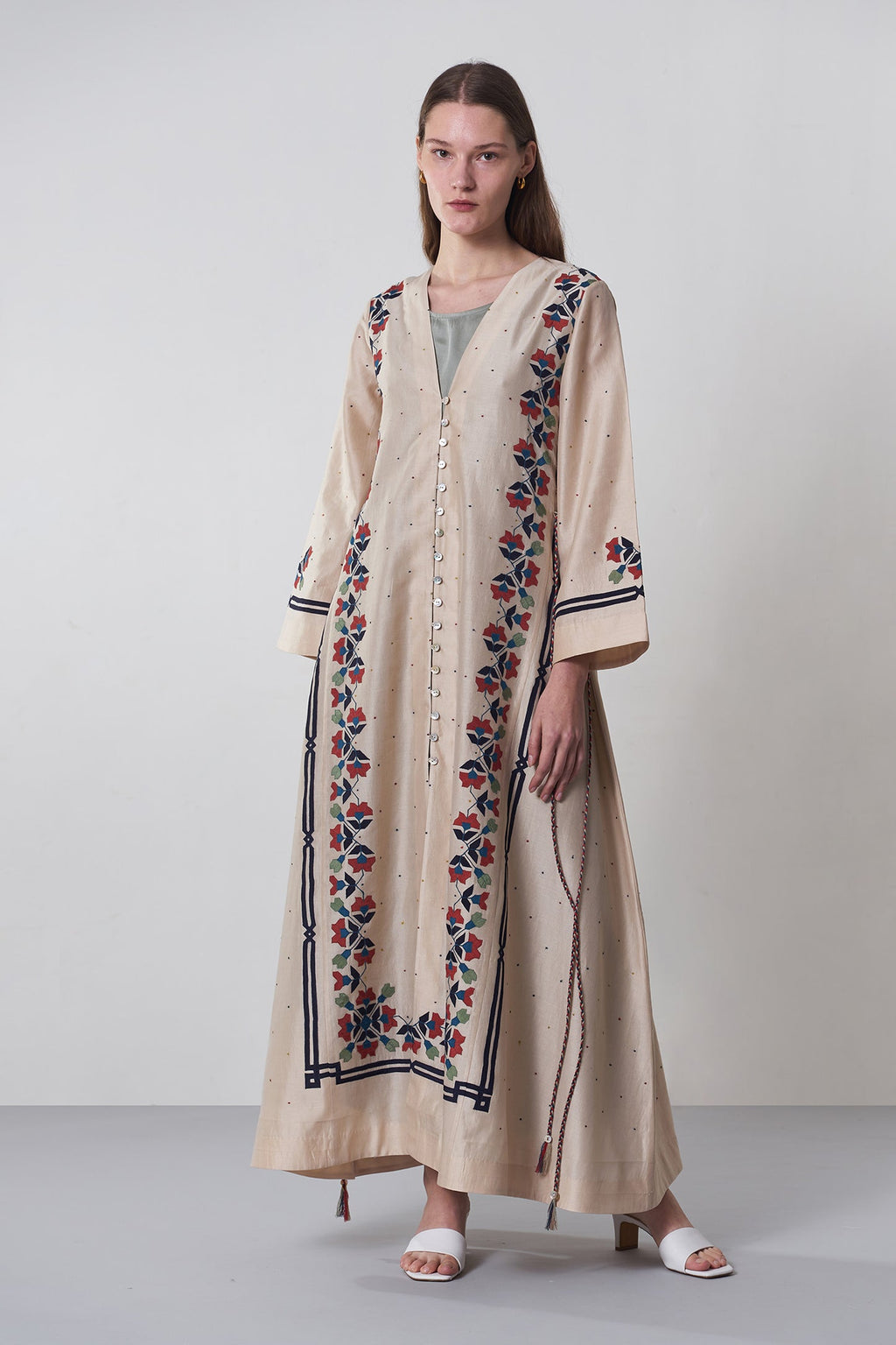 Woman wearing a long embroidered dress on a plain background