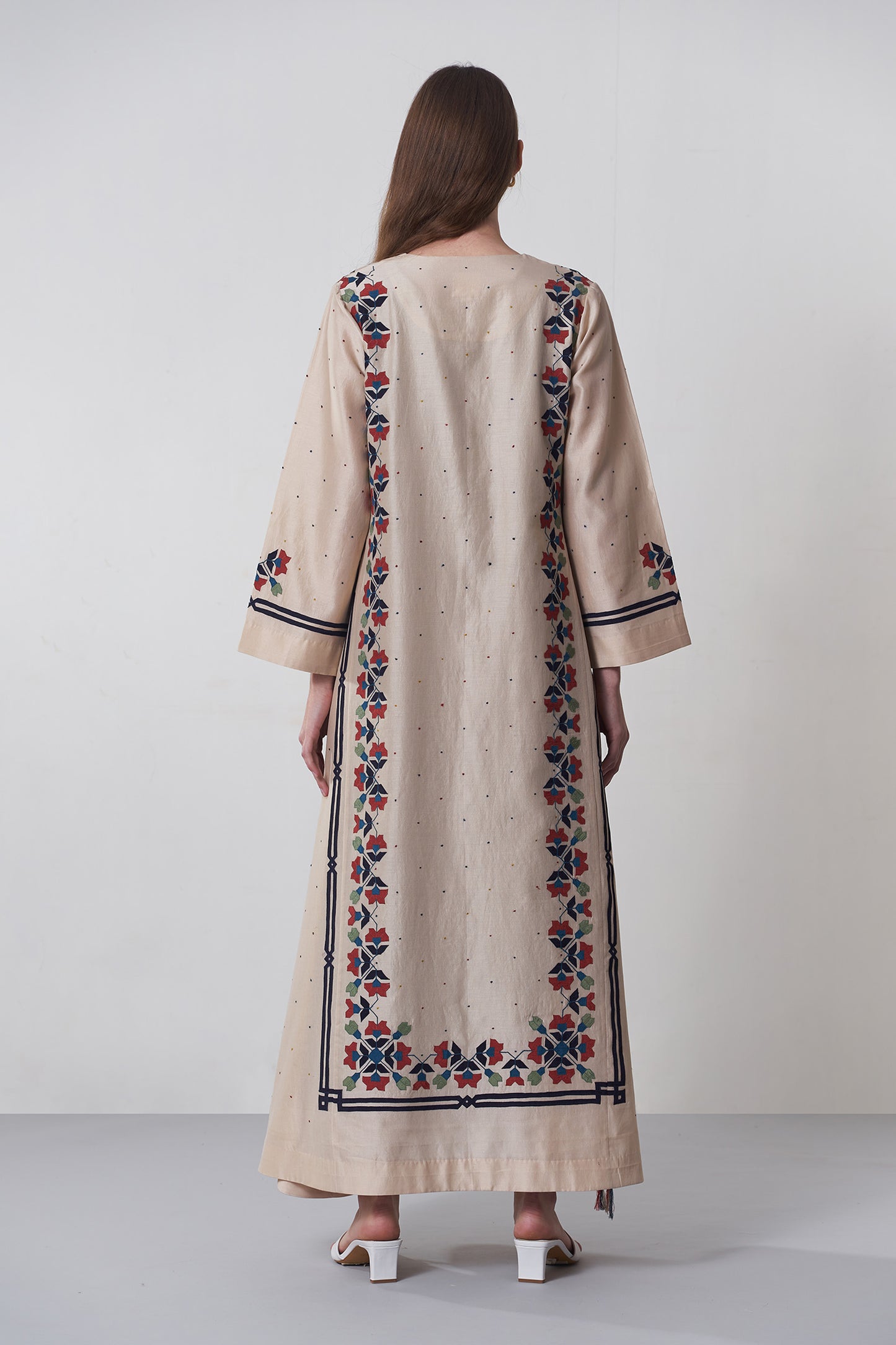 Woman wearing a beige dress with floral embroidery on a plain background