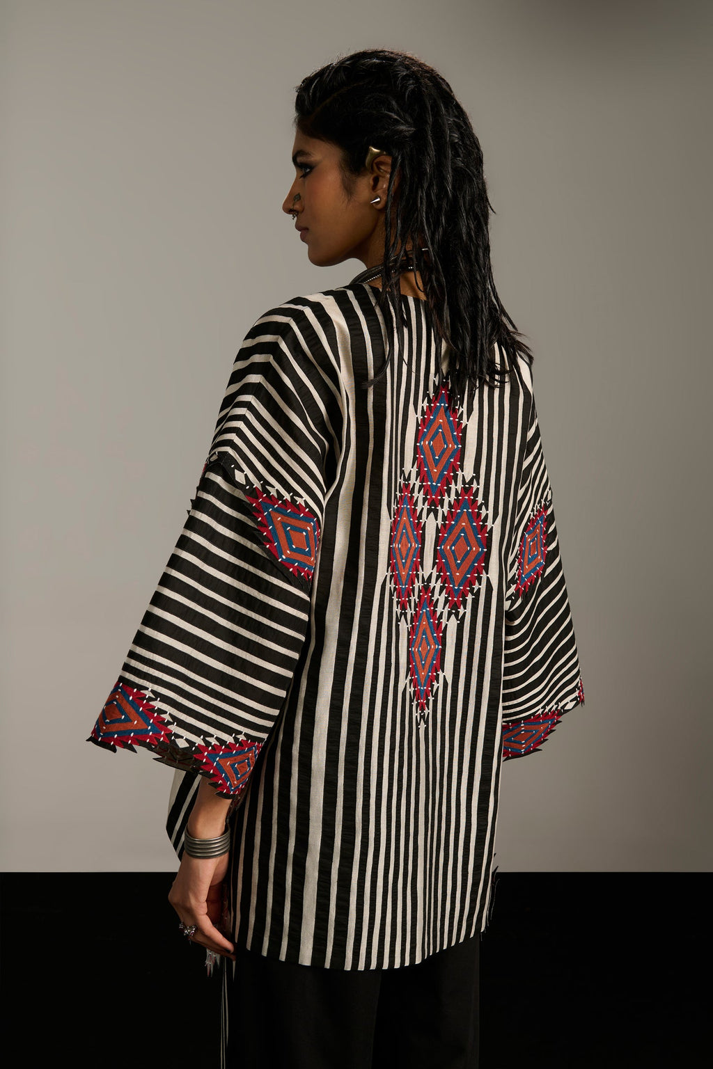 Woman wearing a black and white striped top with colorful embroidery on a plain background