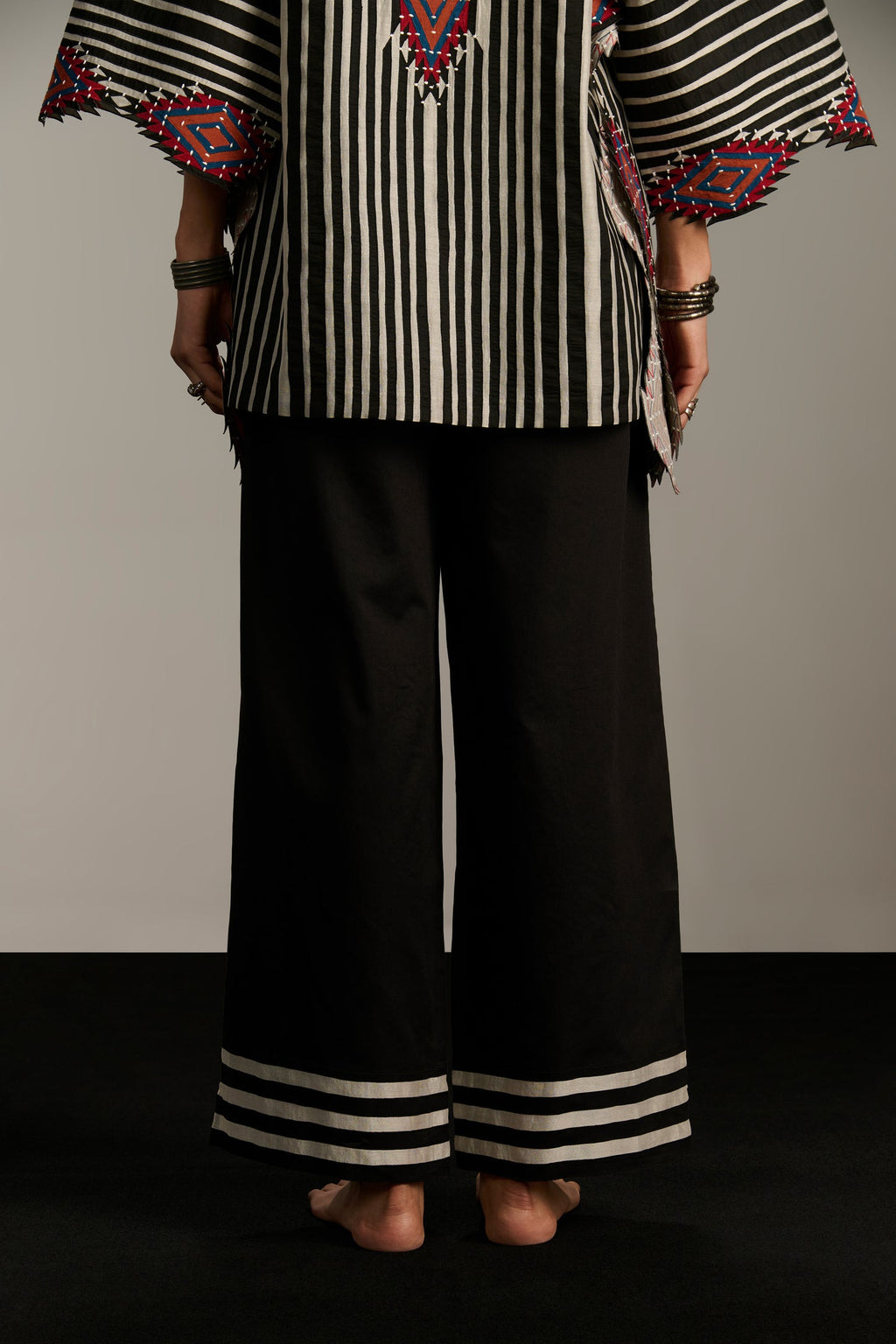 Person wearing a black and white striped top with colorful patterns and black pants on a gray background