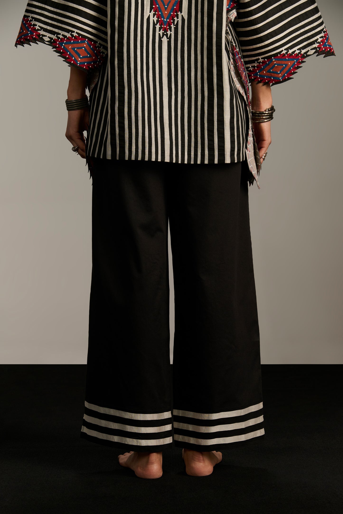 Person wearing a black and white striped top with colorful patterns and black pants on a gray background