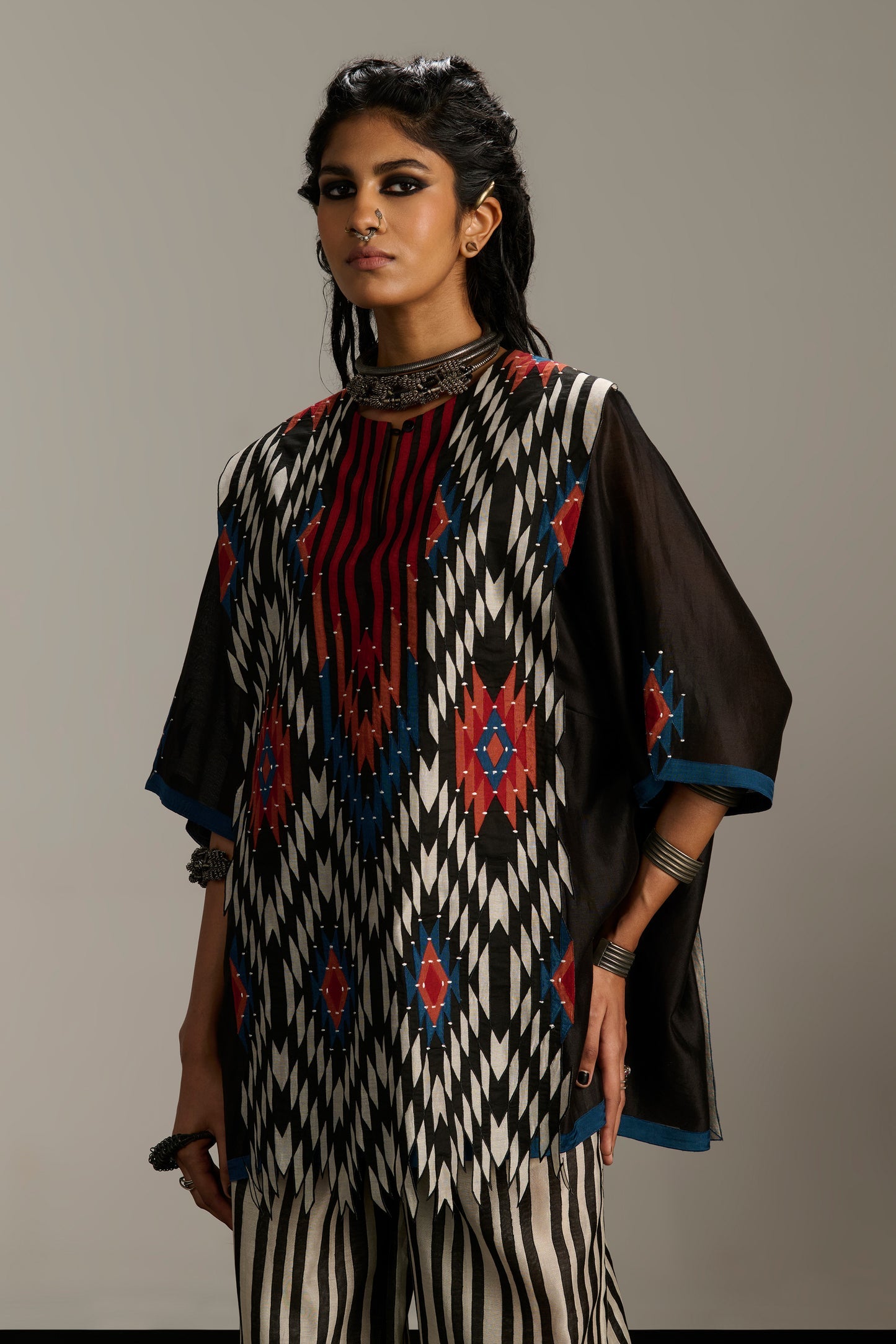 Woman wearing a traditional outfit with black, white, and red patterns on a gray background