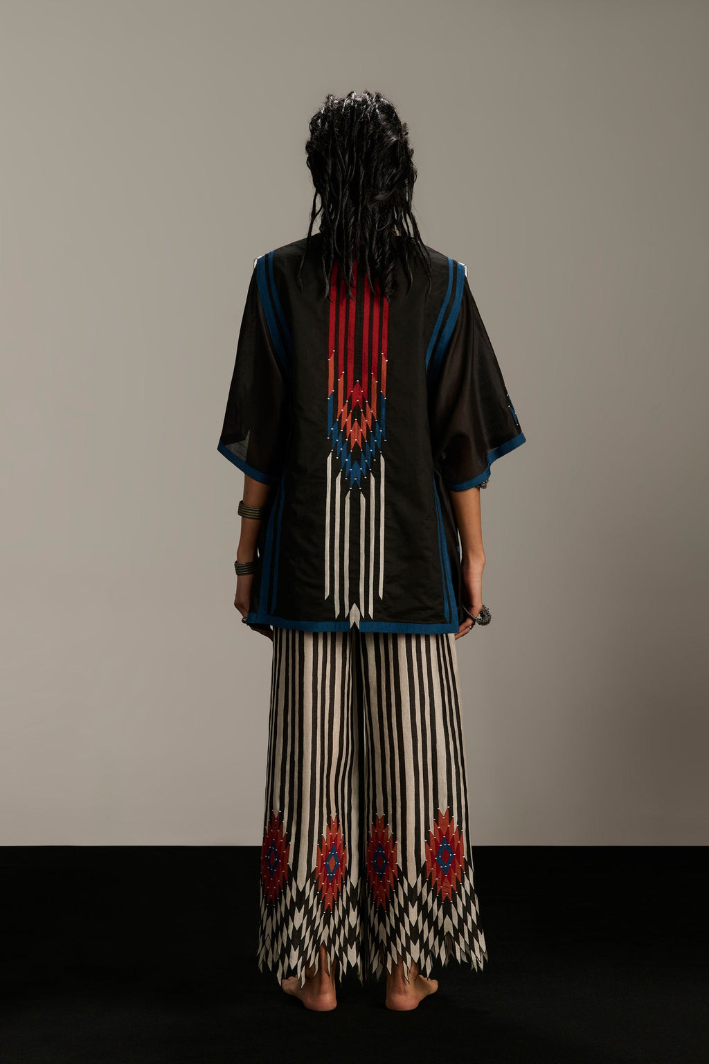 Person wearing a traditional outfit with a black top and patterned skirt on a plain background