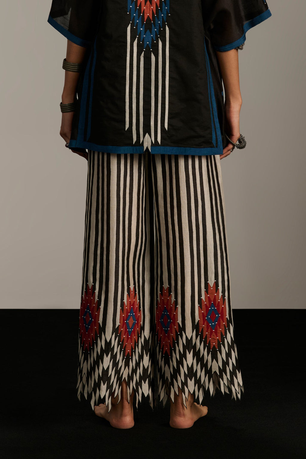 Person wearing a black top with blue and red patterns and striped pants with geometric designs.