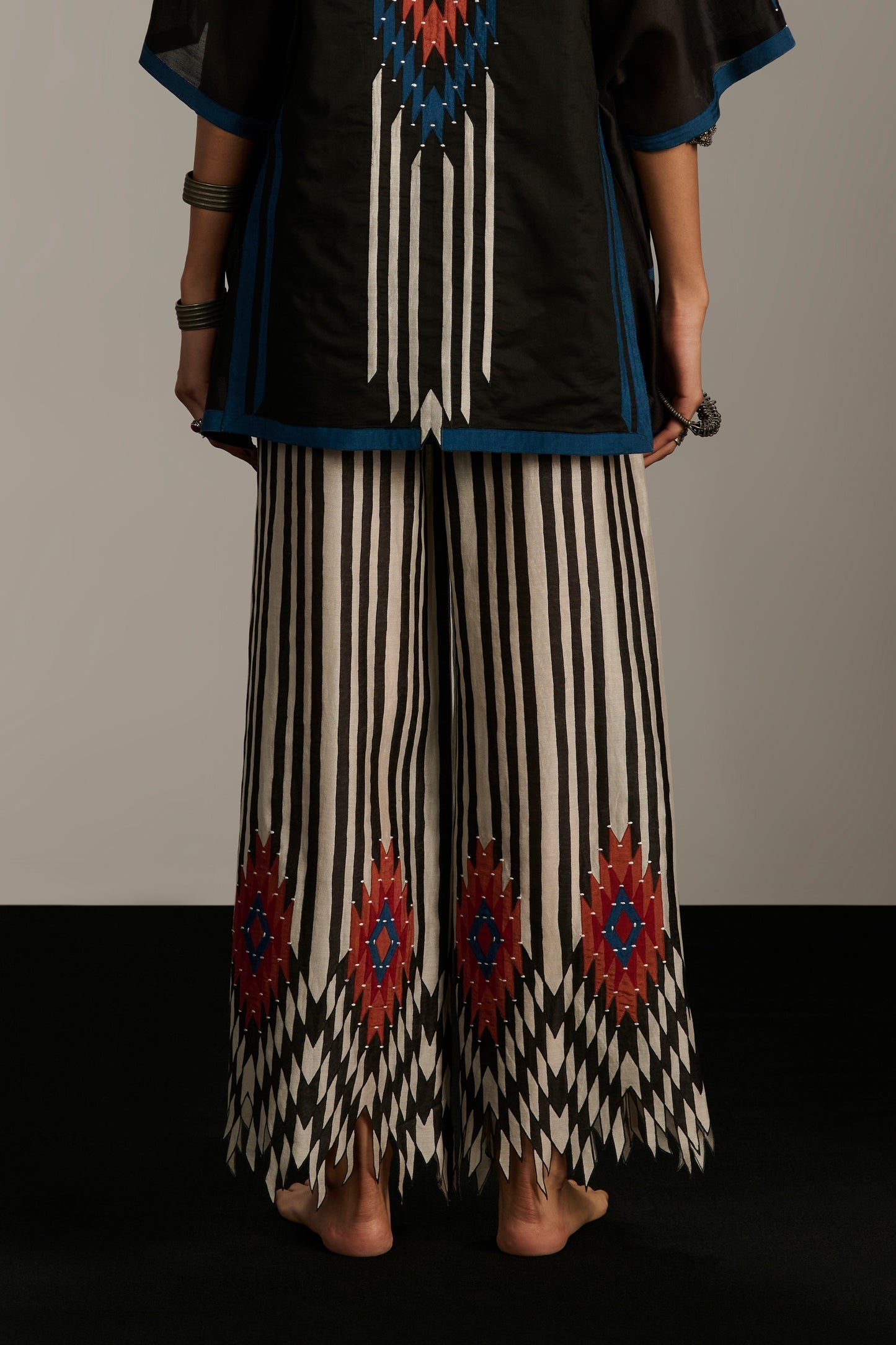 Person wearing a black top with blue and red patterns and striped pants with geometric designs.