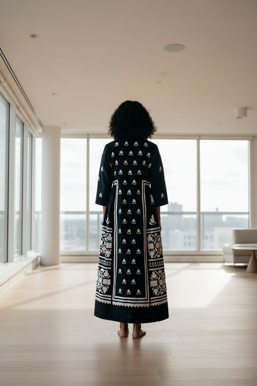 Person wearing a black dress with white patterns on a red floor and black background