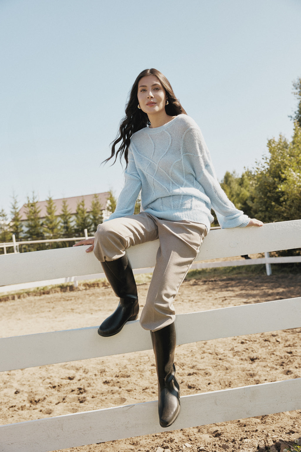 Woman sitting on a white fence in an equestrian setting