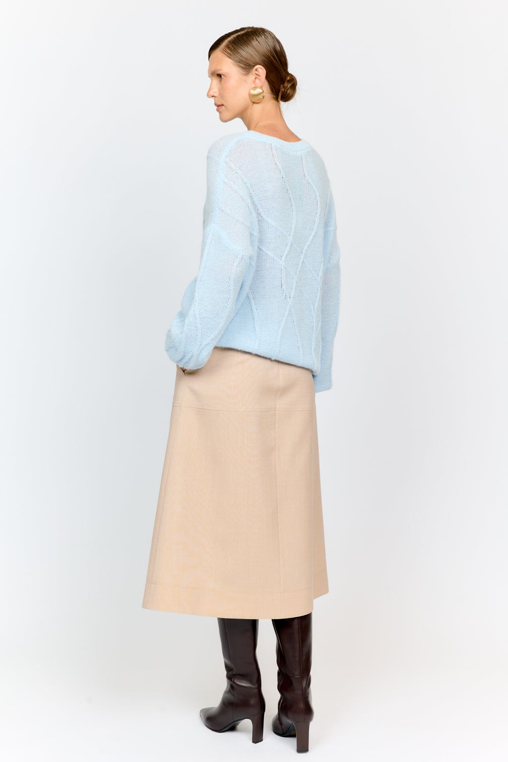 Woman wearing a light blue sweater, beige skirt, and brown boots on a white background