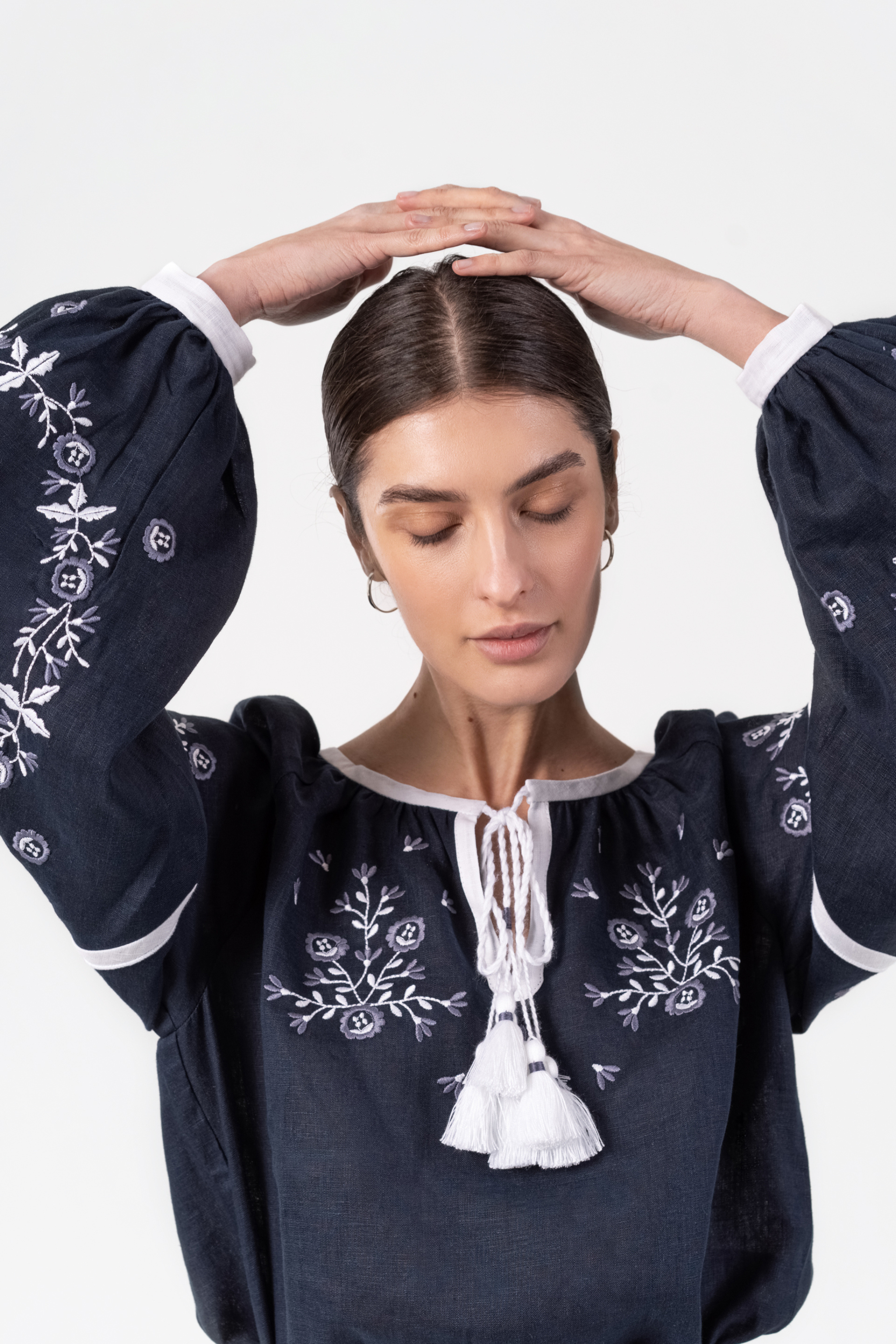 Woman wearing a navy blue embroidered blouse with white details on a white background