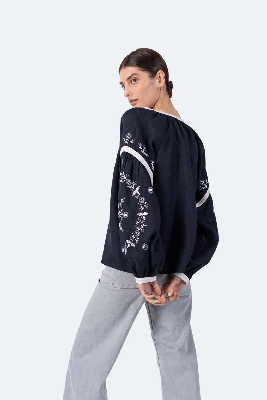 Person wearing a black embroidered jacket with white pants on a white background