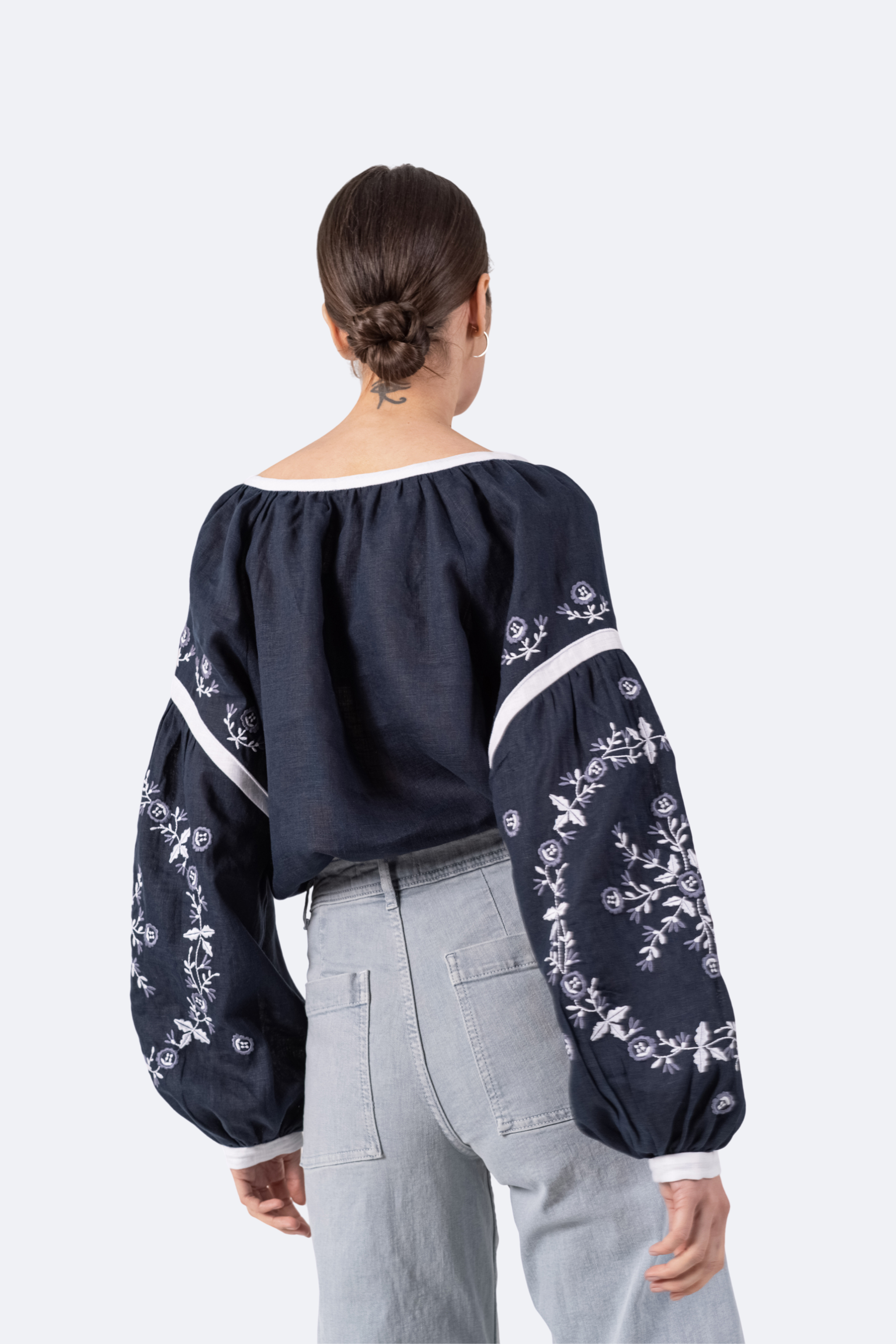 Person wearing a navy blue blouse with white floral embroidery on a light gray background