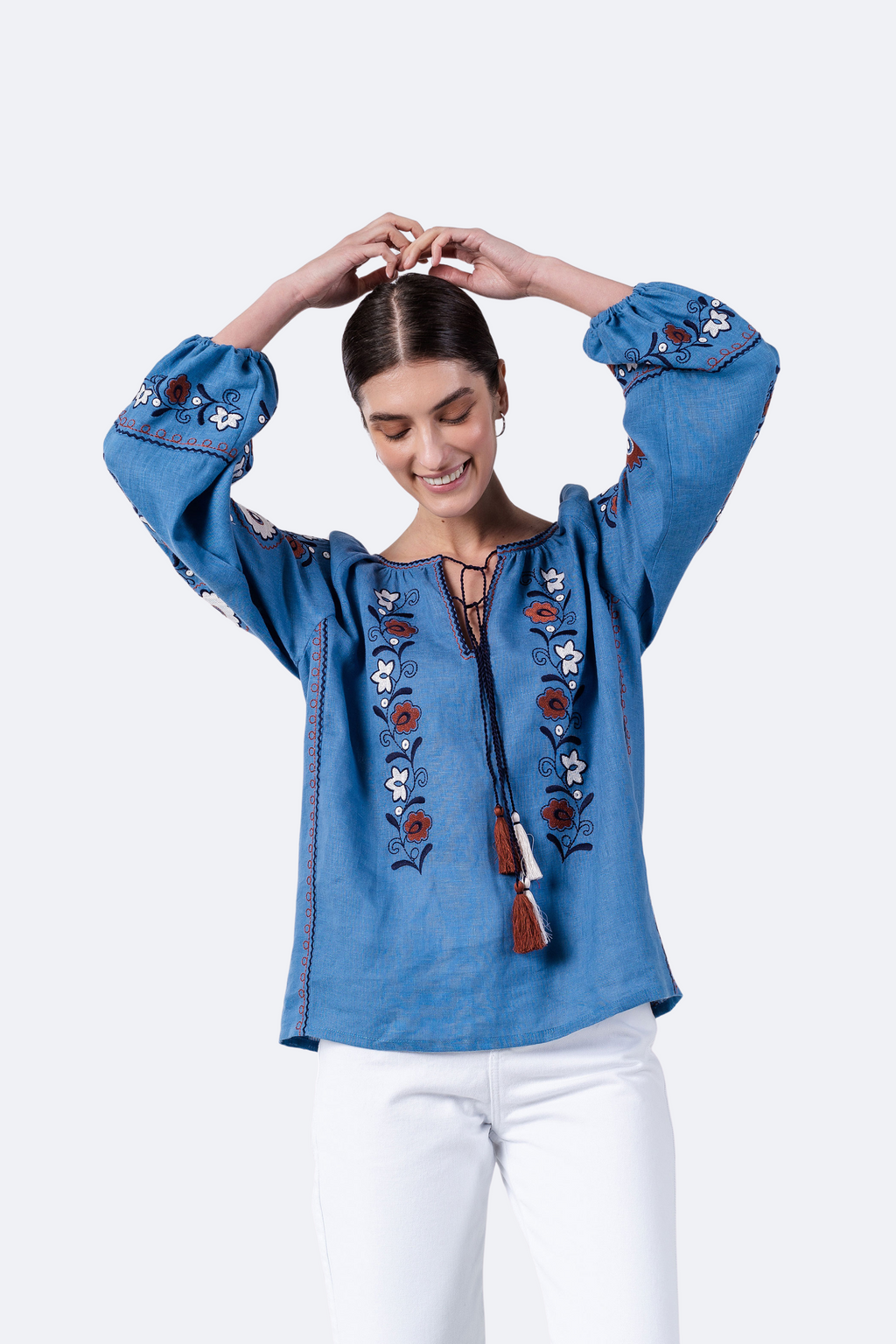 Woman wearing a blue embroidered blouse with white pants on a white background