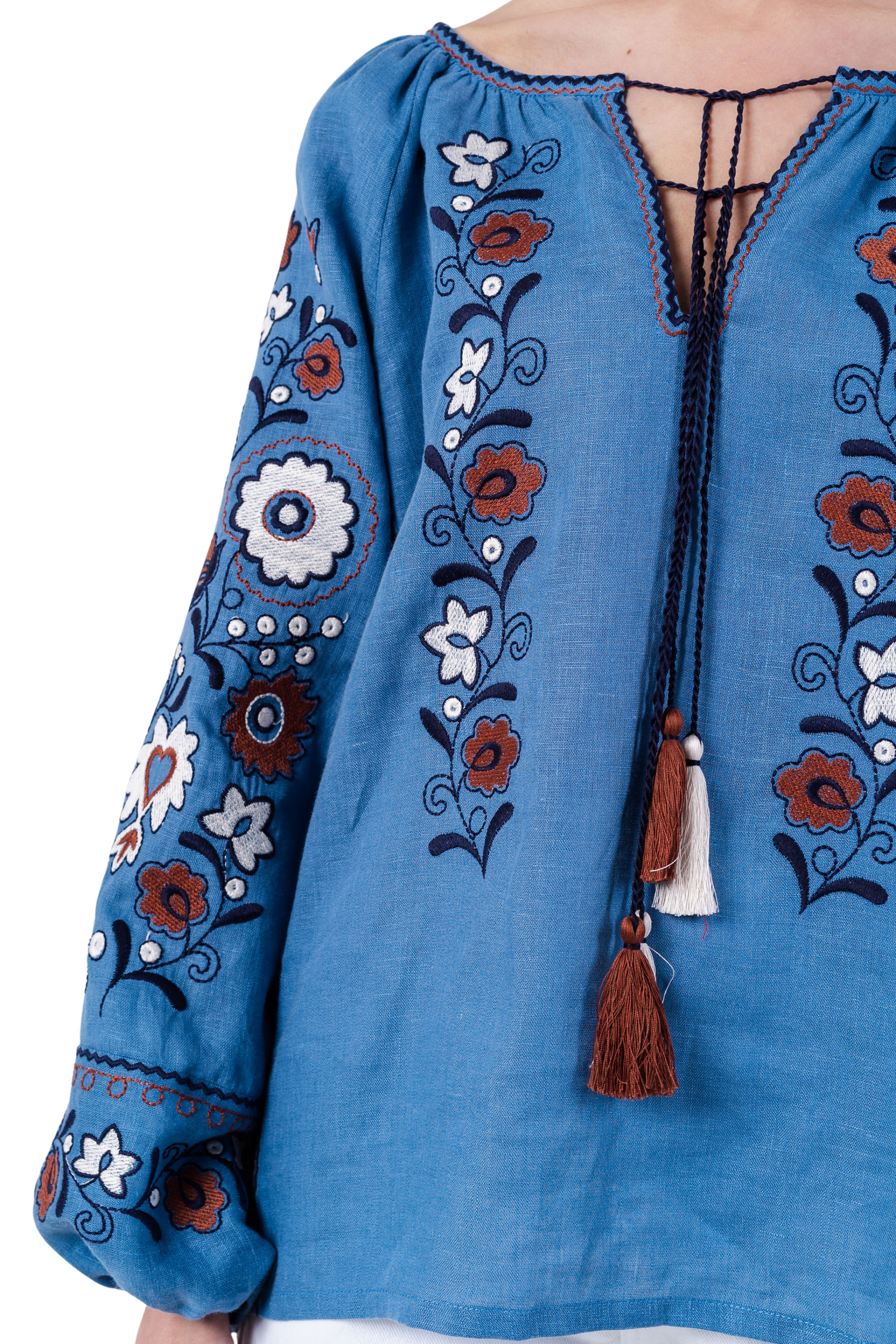 Blue embroidered blouse with floral patterns and tassels on a white background