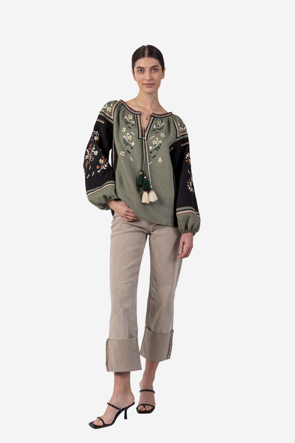 Woman wearing an embroidered top and beige pants on a white background