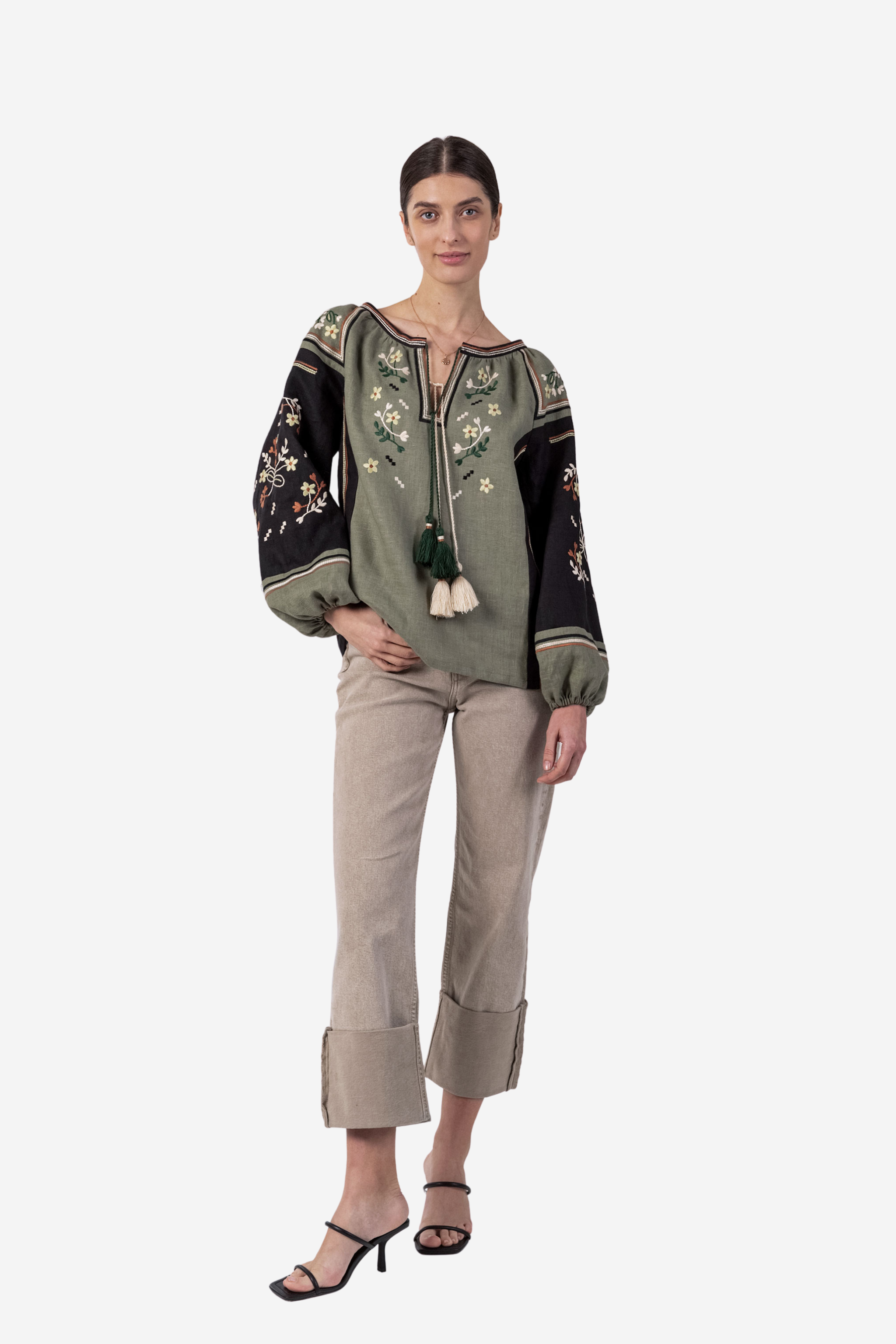 Woman wearing an embroidered top and beige pants on a white background