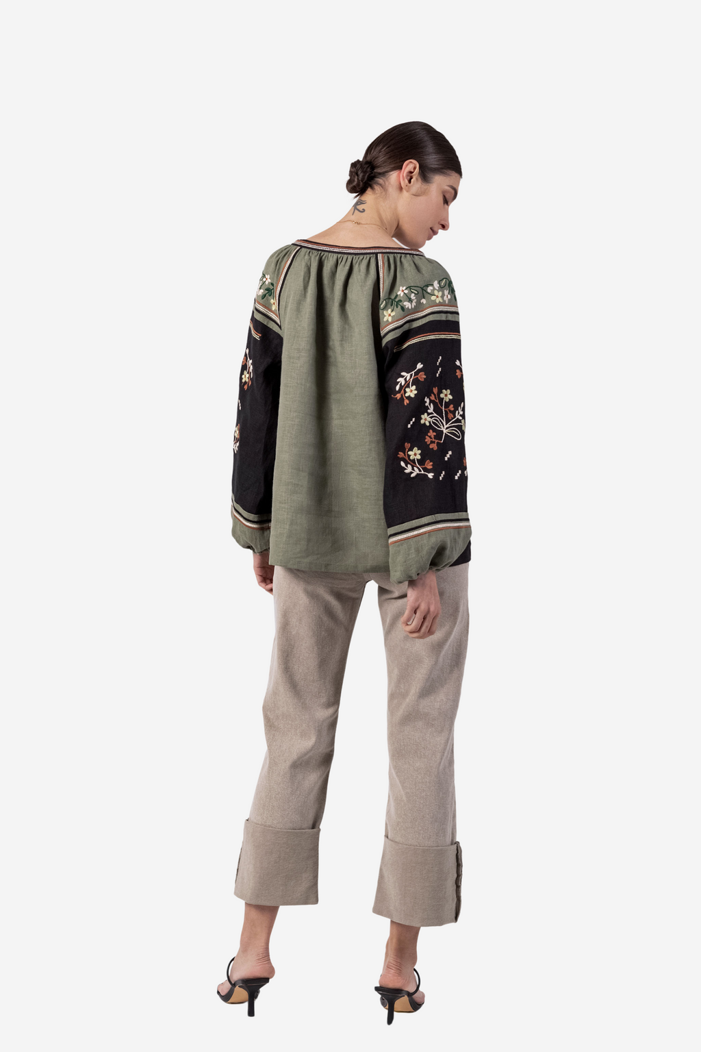 Woman wearing a green and black embroidered blouse with beige pants on a white background
