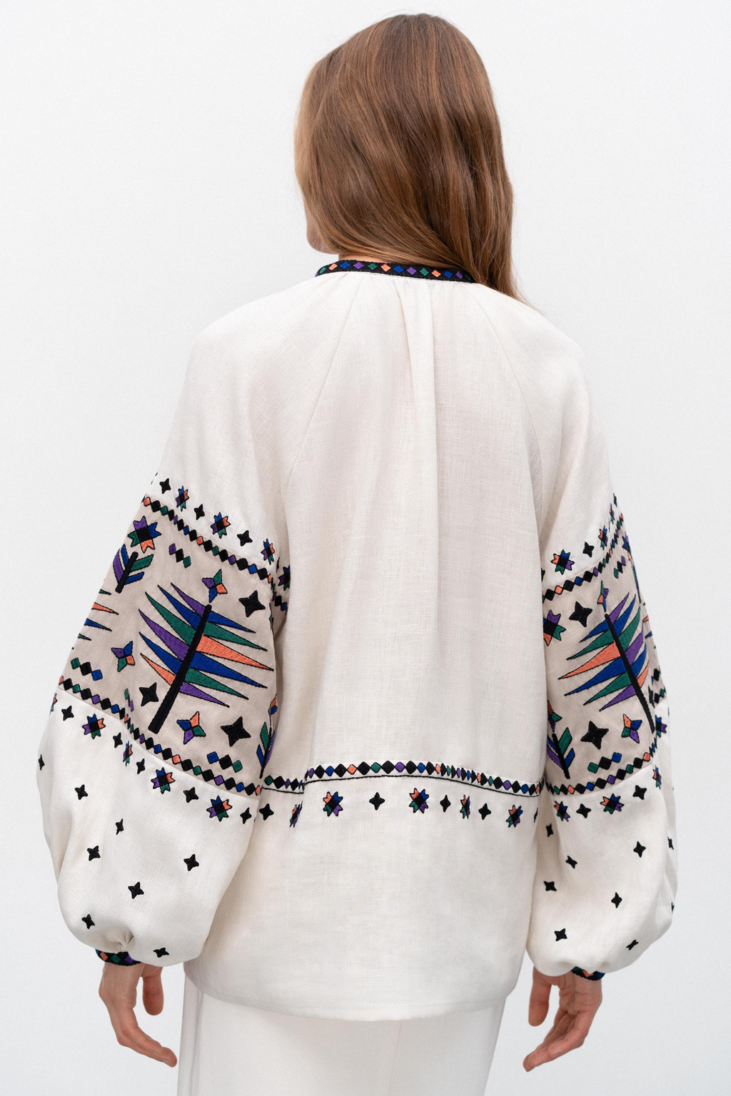 White blouse with colorful embroidery on sleeves and back, worn by a person.