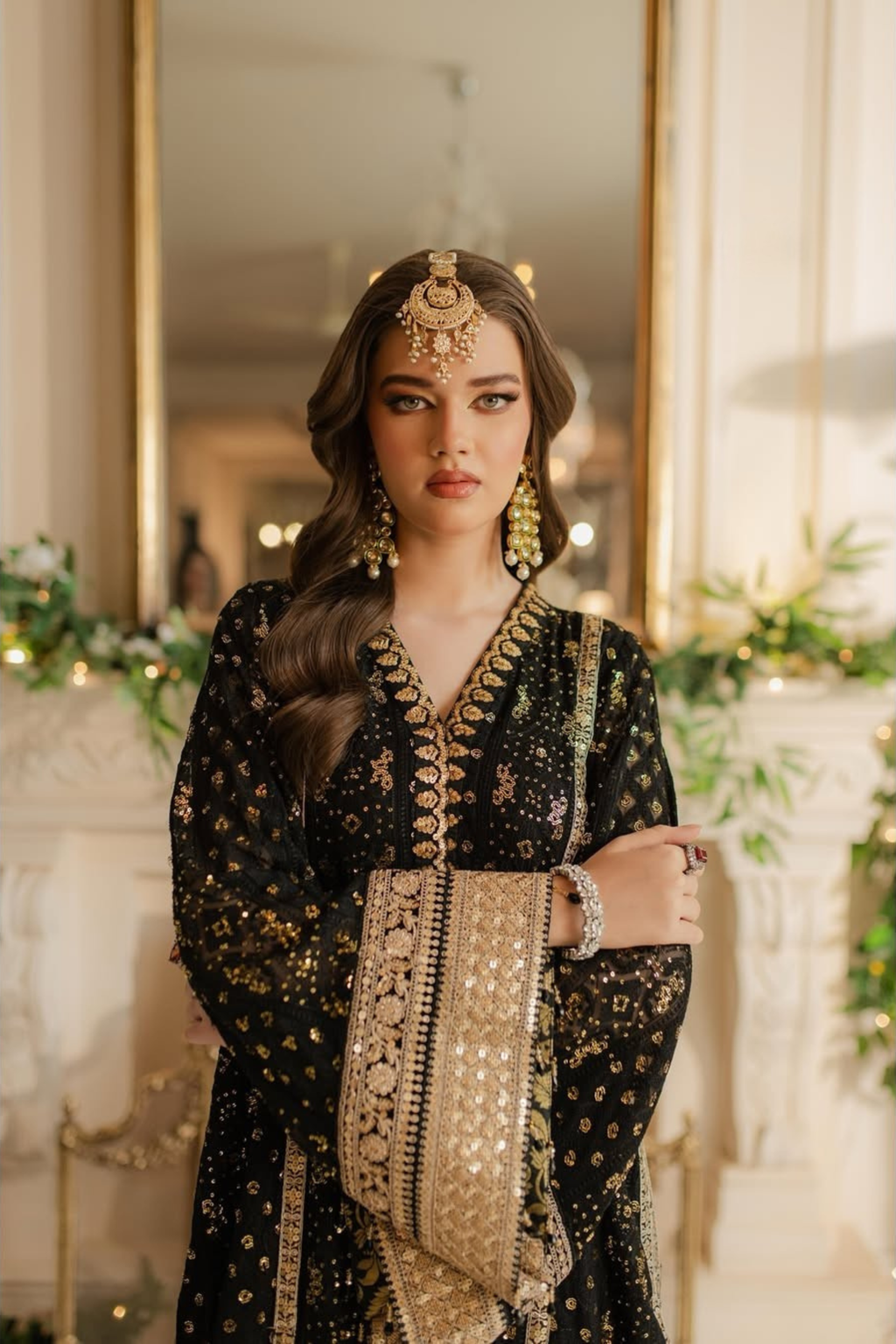 Woman in traditional black and gold embroidered outfit with jewelry in a decorated indoor setting