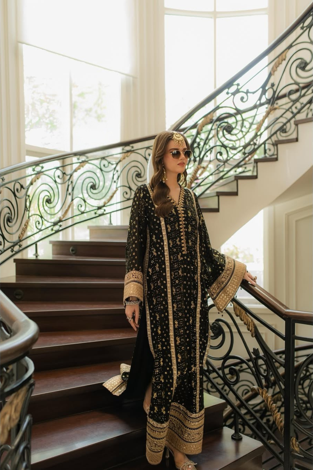 Woman in a black and gold dress standing on a staircase with decorative railings.