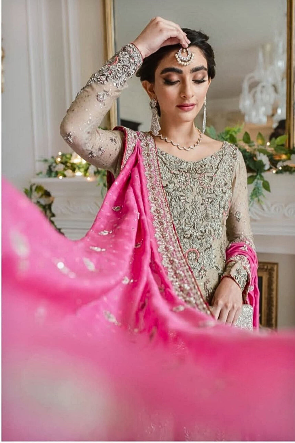 Woman in traditional attire with pink fabric, indoors with decorative elements.