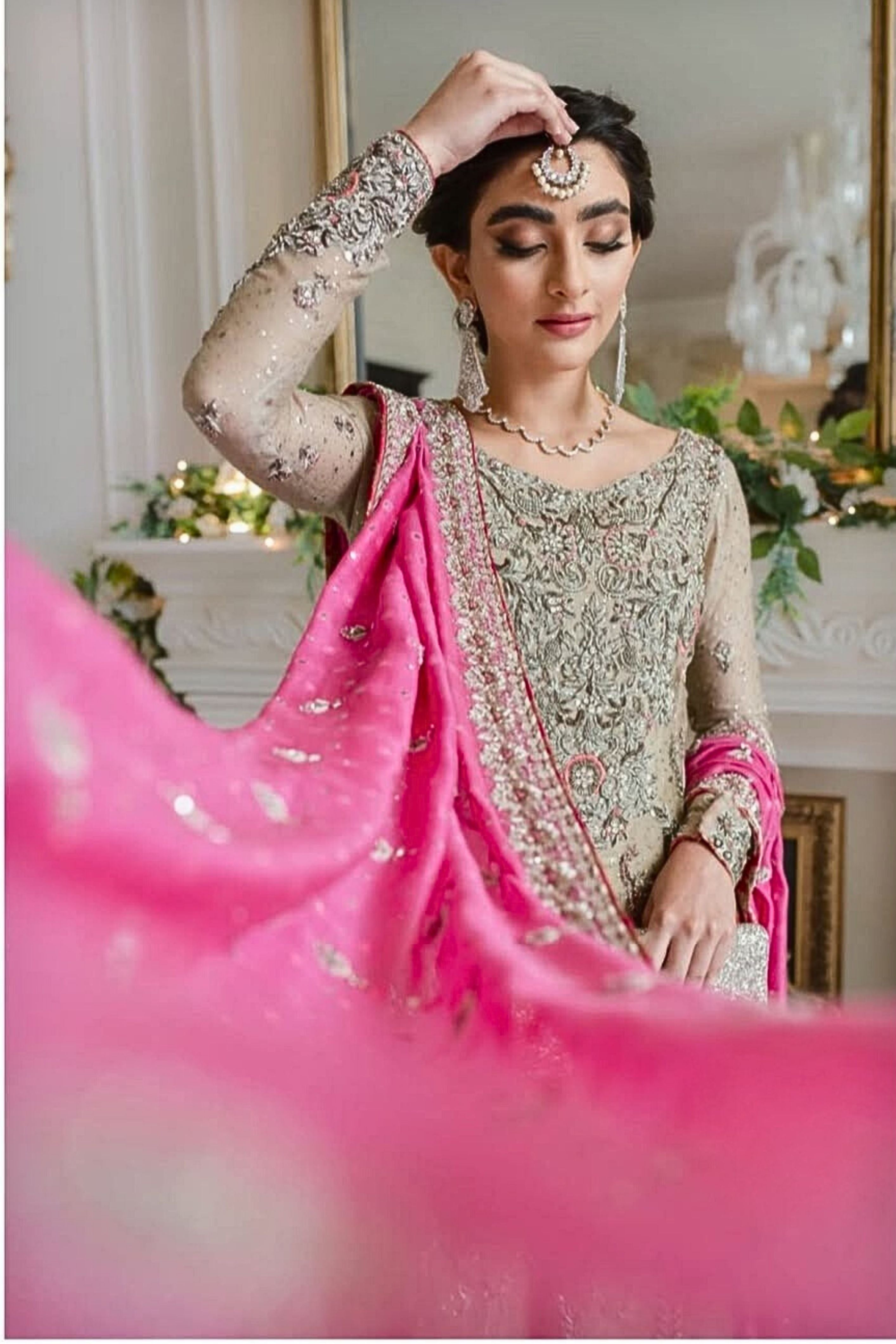 Woman in traditional attire with pink fabric, indoors with decorative elements.
