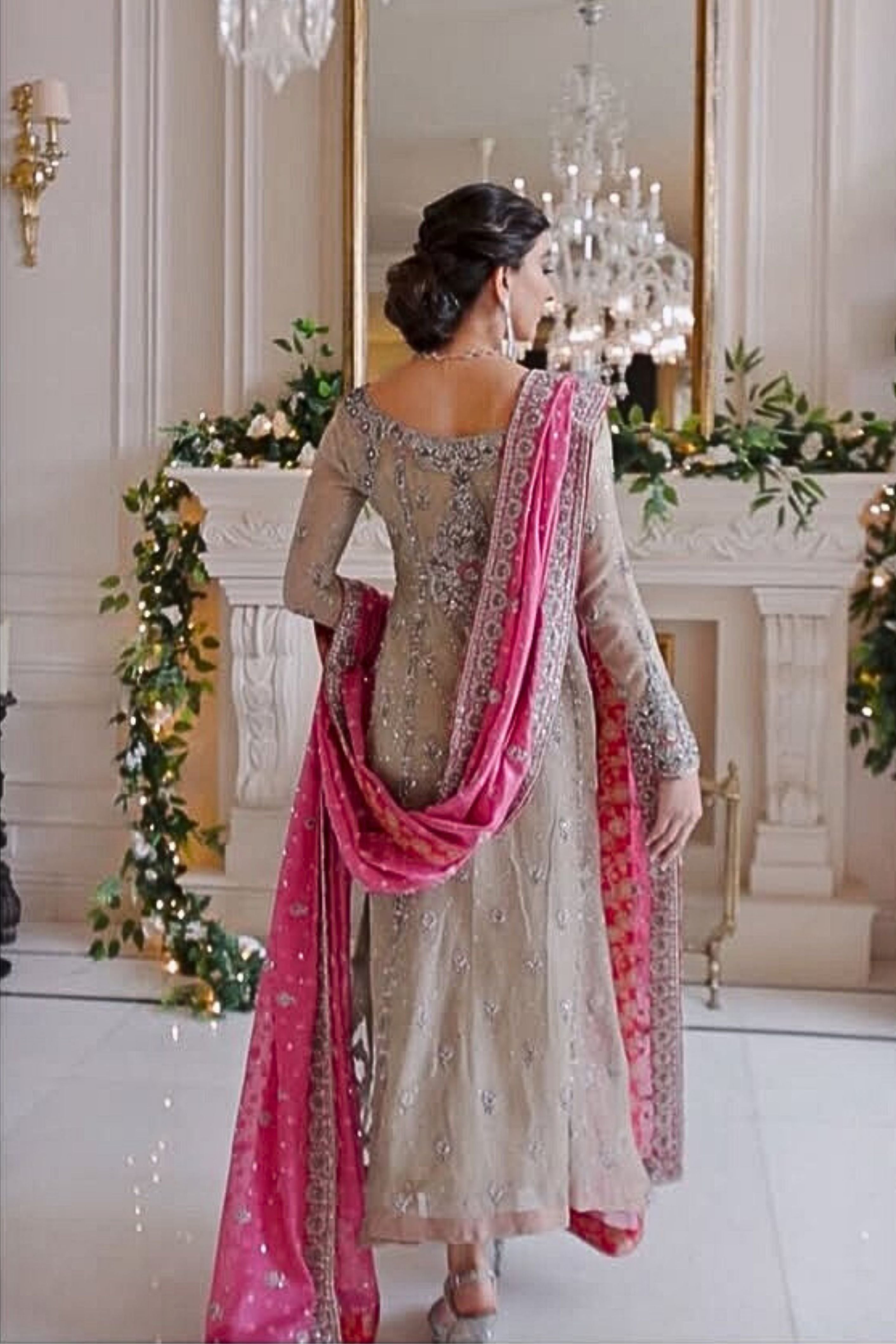 Woman in a traditional outfit with a pink dupatta standing in a decorated room.