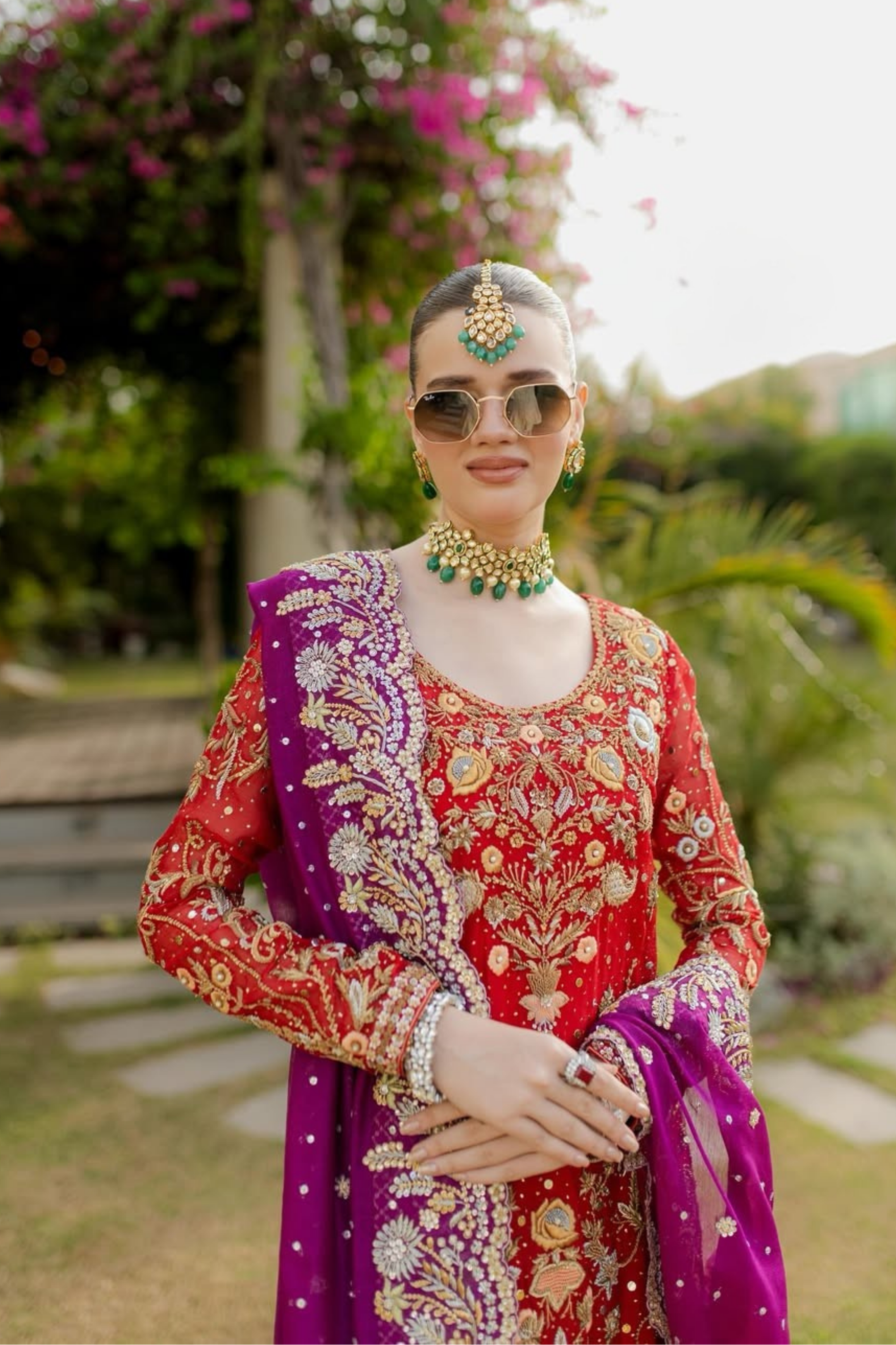 Woman in traditional red and purple outfit with jewelry and sunglasses outdoors.
