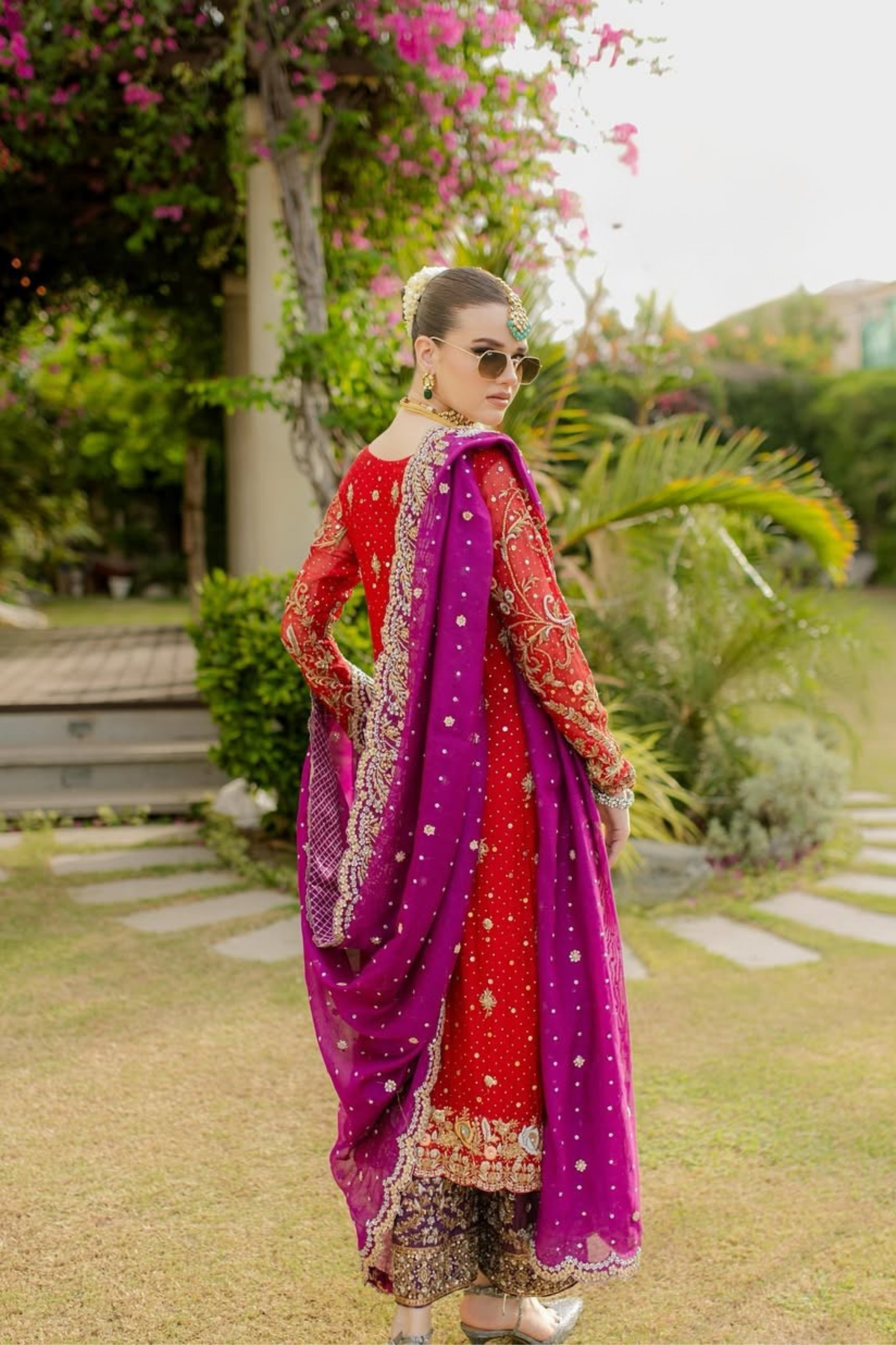 Woman in a red and purple traditional outfit standing outdoors with greenery in the background