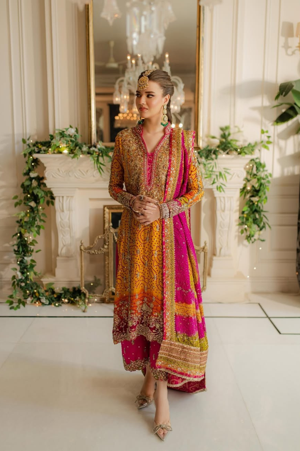 Woman in a colorful traditional outfit standing in an elegant room with decorative elements.