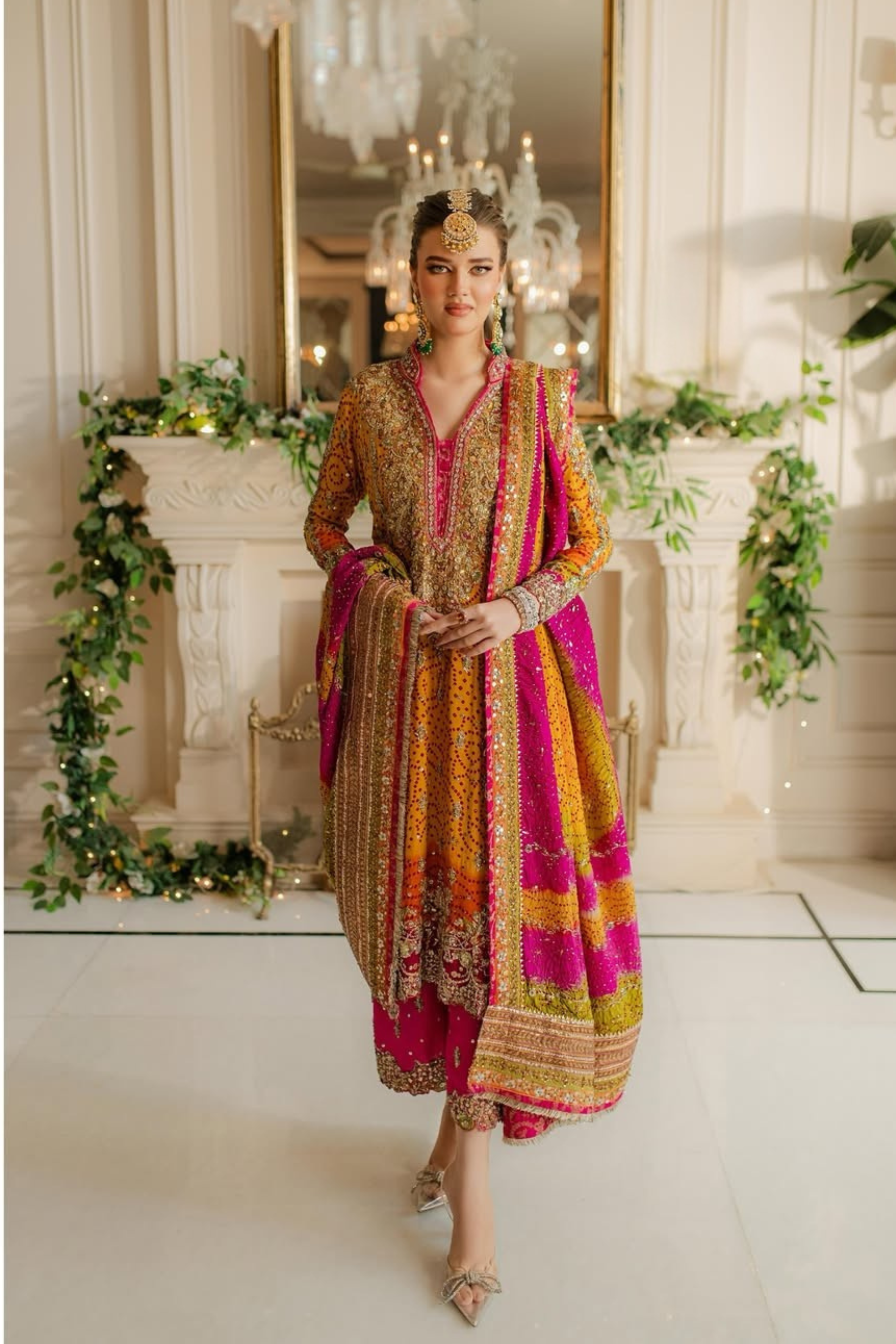 Woman in a colorful traditional outfit standing in an elegant room with decorative elements.