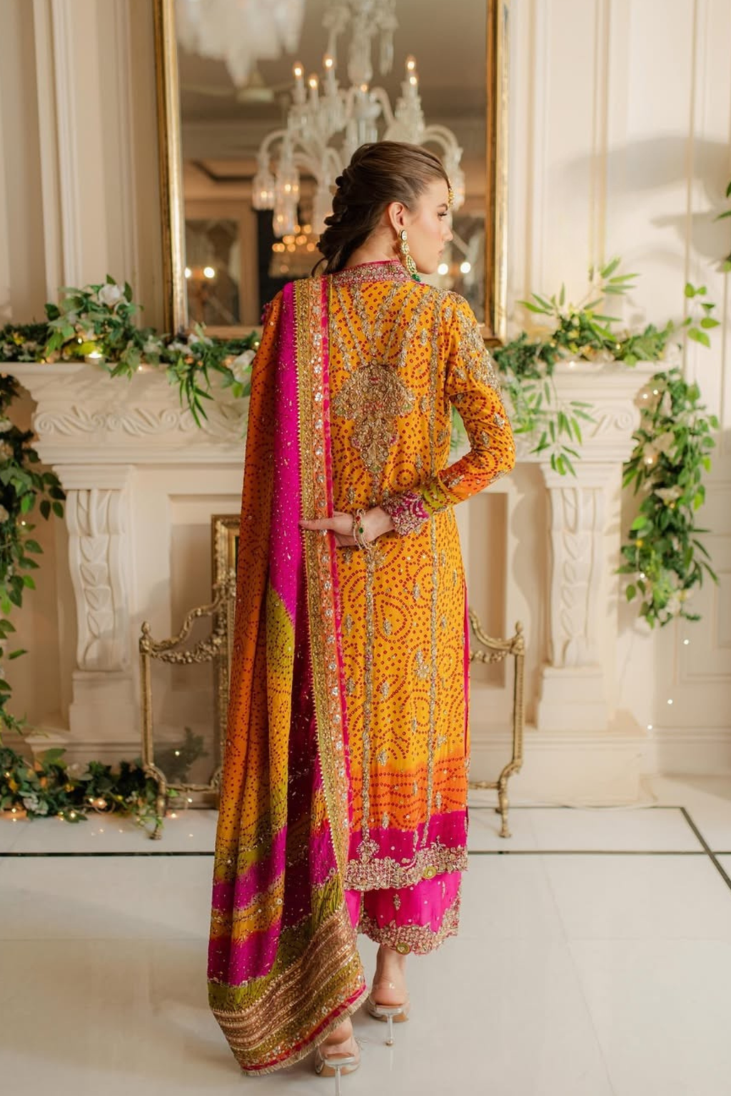 Woman in a traditional outfit with intricate patterns standing in a decorated room.