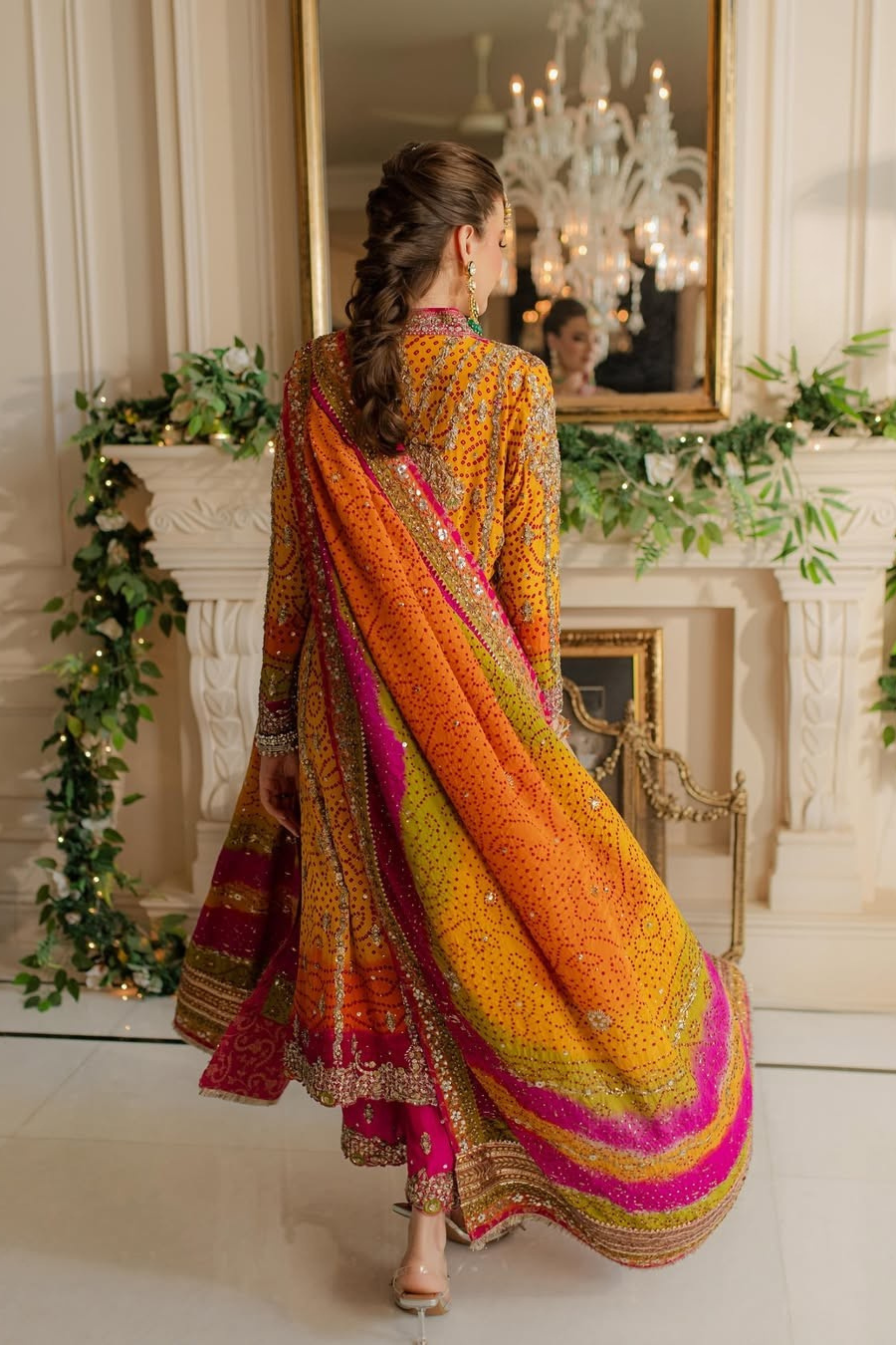 Woman in a colorful traditional outfit standing in a decorated room with a chandelier.