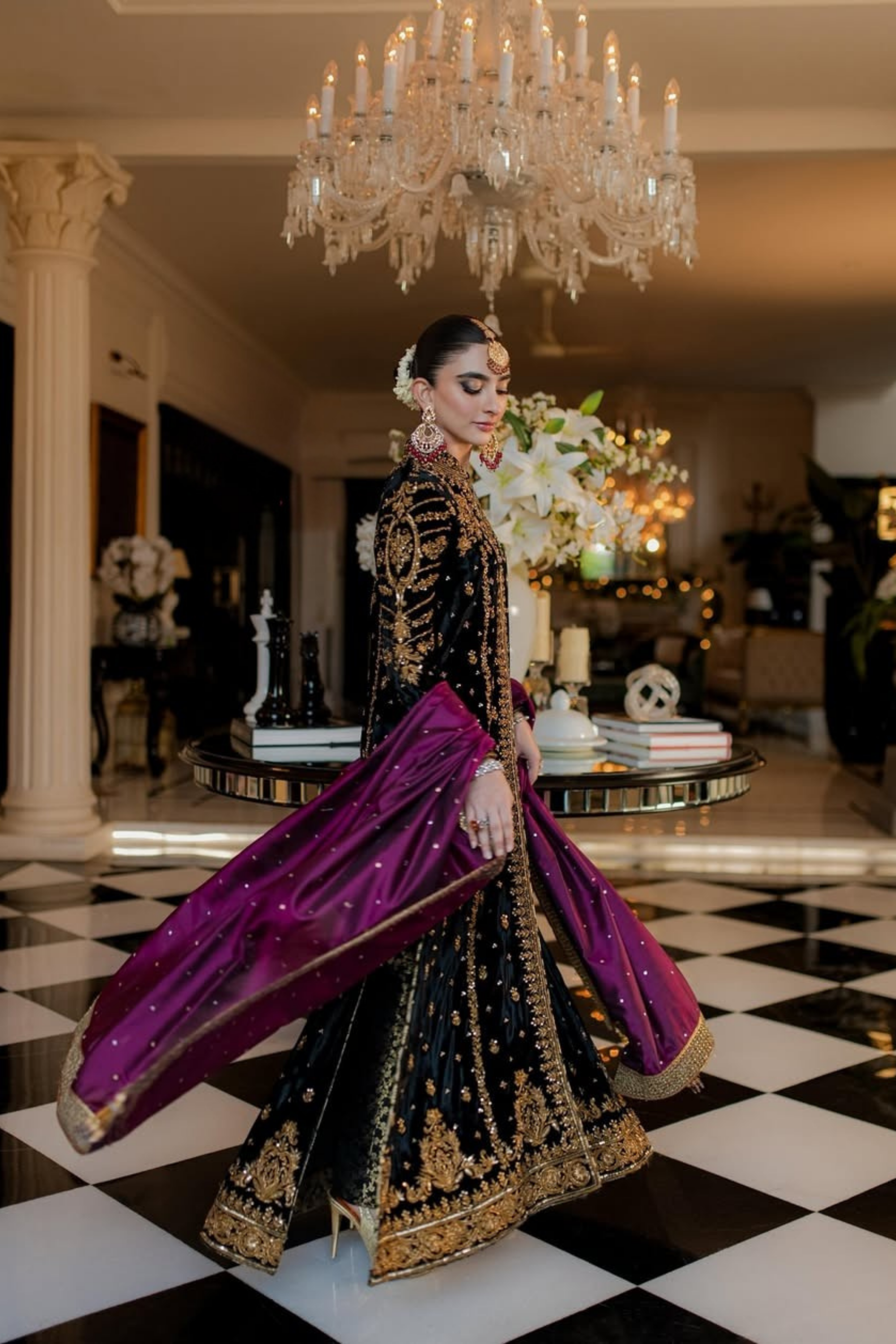 Woman in a traditional outfit with a purple dupatta in an elegant indoor setting.