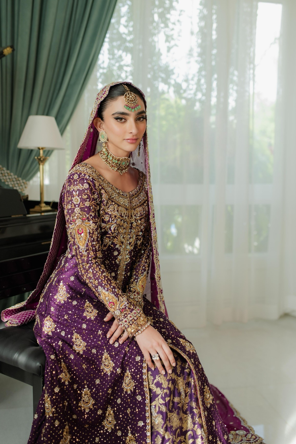 Woman in a purple and gold traditional outfit with intricate designs, sitting indoors.