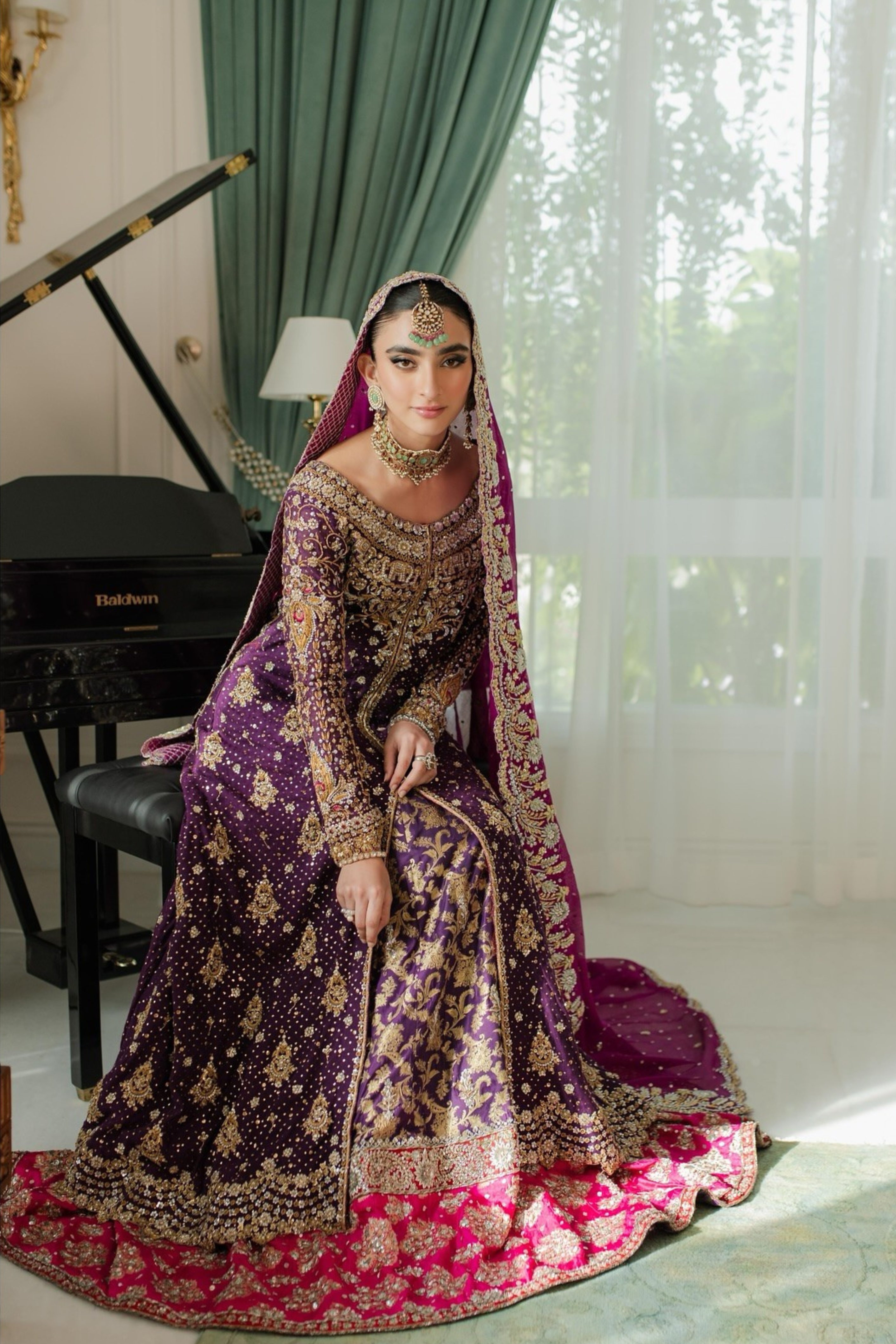 Woman in traditional purple and gold outfit sitting in a room with a piano and curtains.