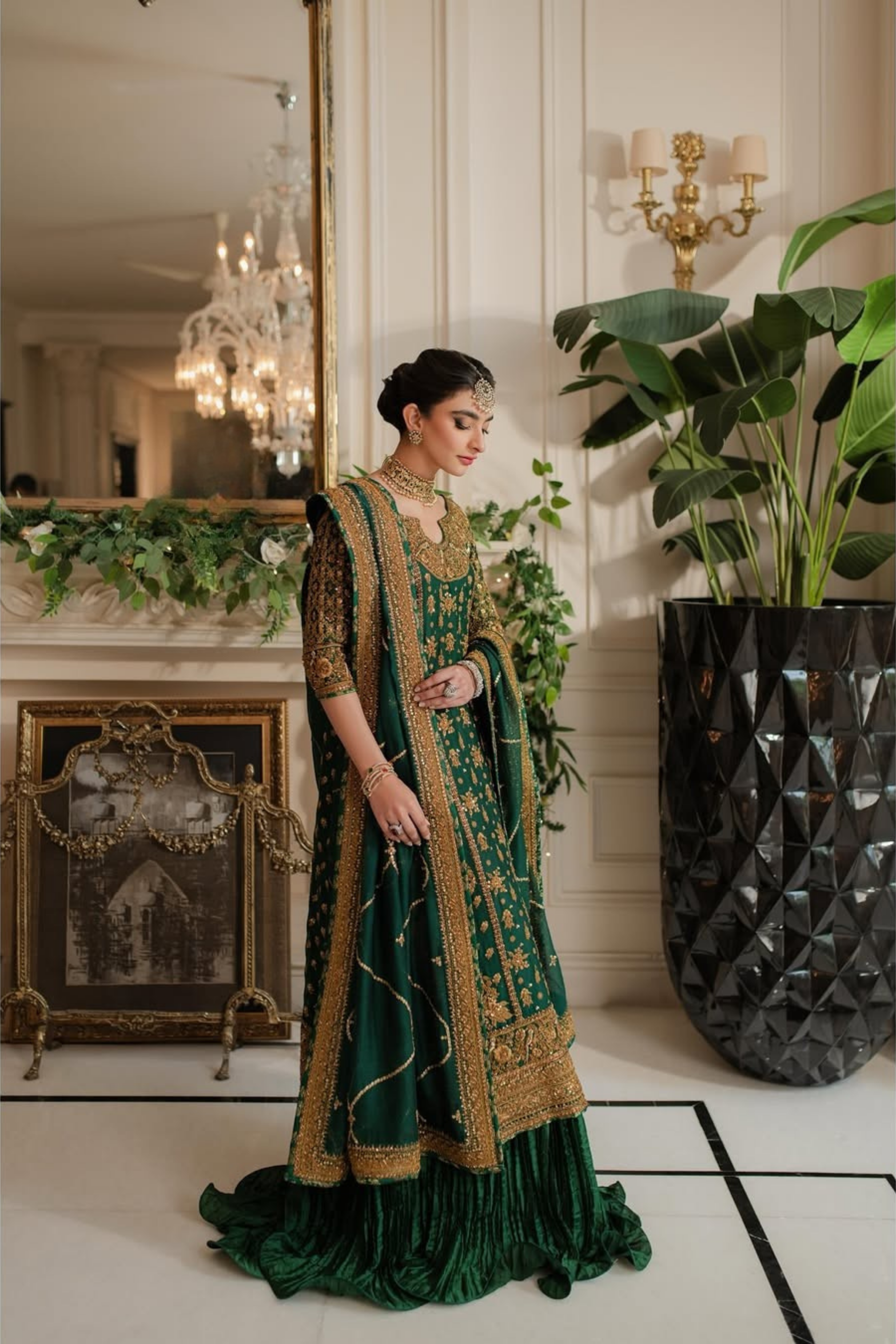Woman in a green and gold traditional outfit standing in an elegant room with decorative elements.
