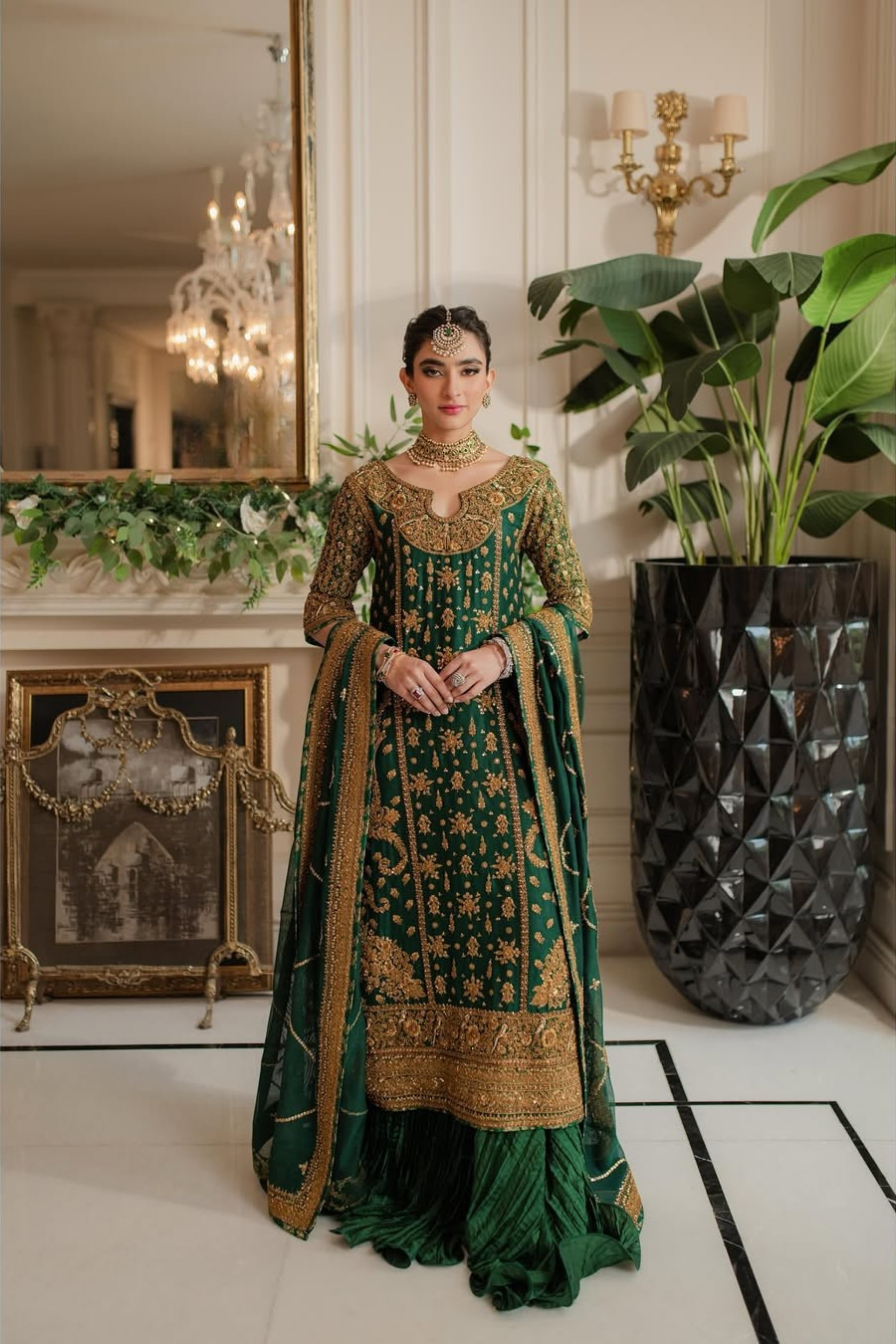 Woman in a green and gold traditional outfit standing in an elegant room with decorative elements.