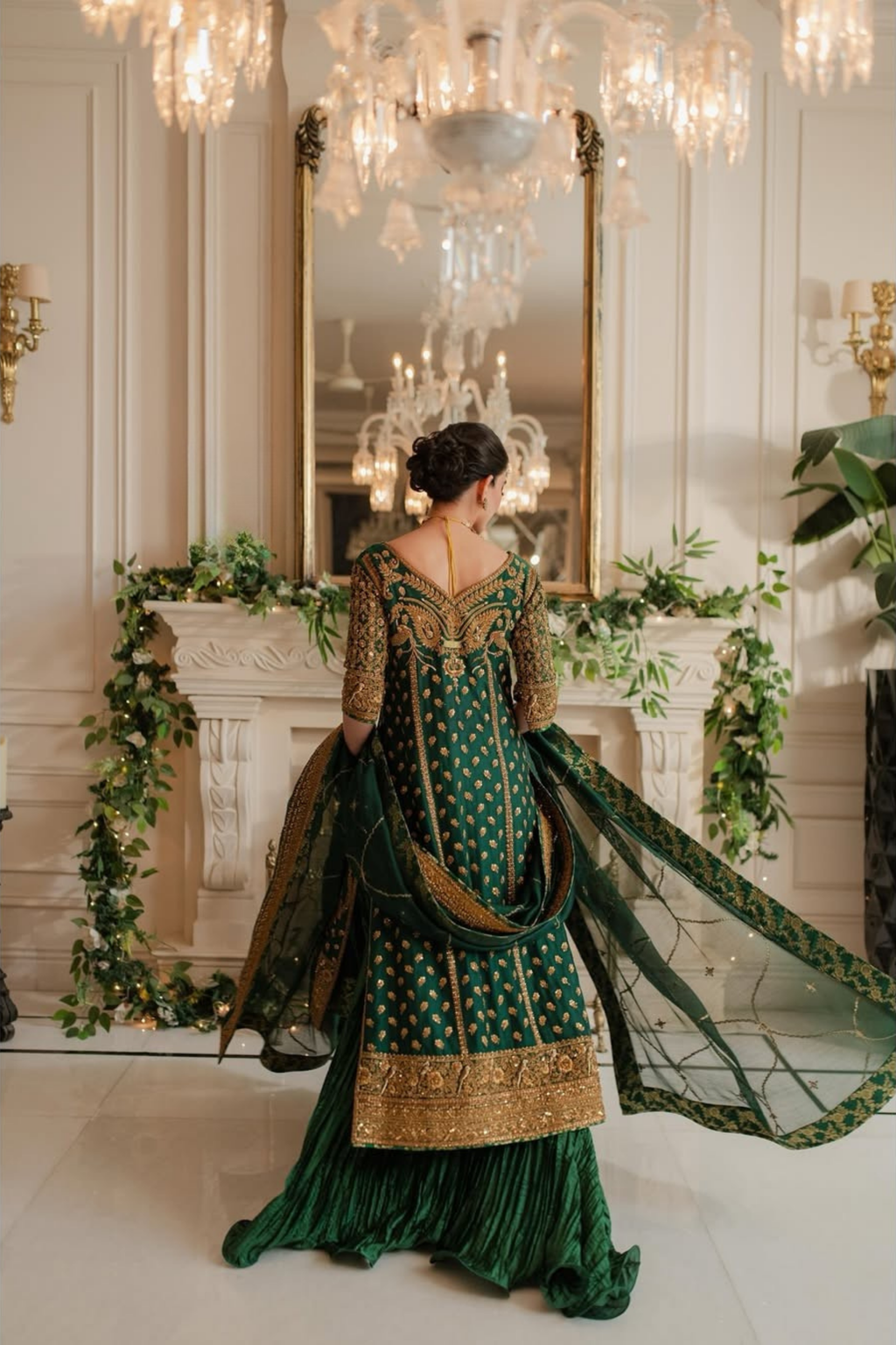 Woman in a green and gold dress standing in an elegant room with chandeliers and decorative elements.