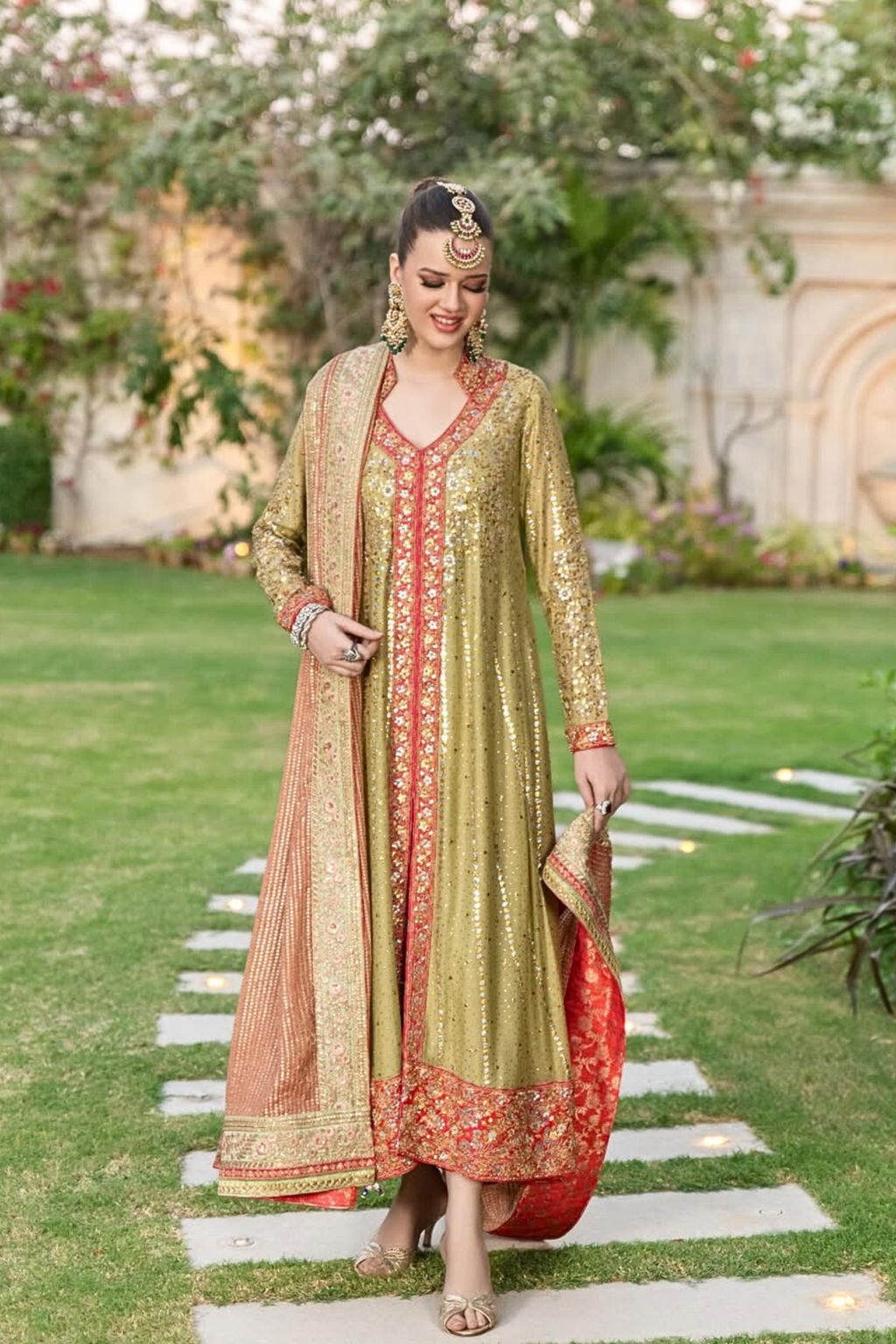 Woman in a green and red traditional outfit standing on a garden path.