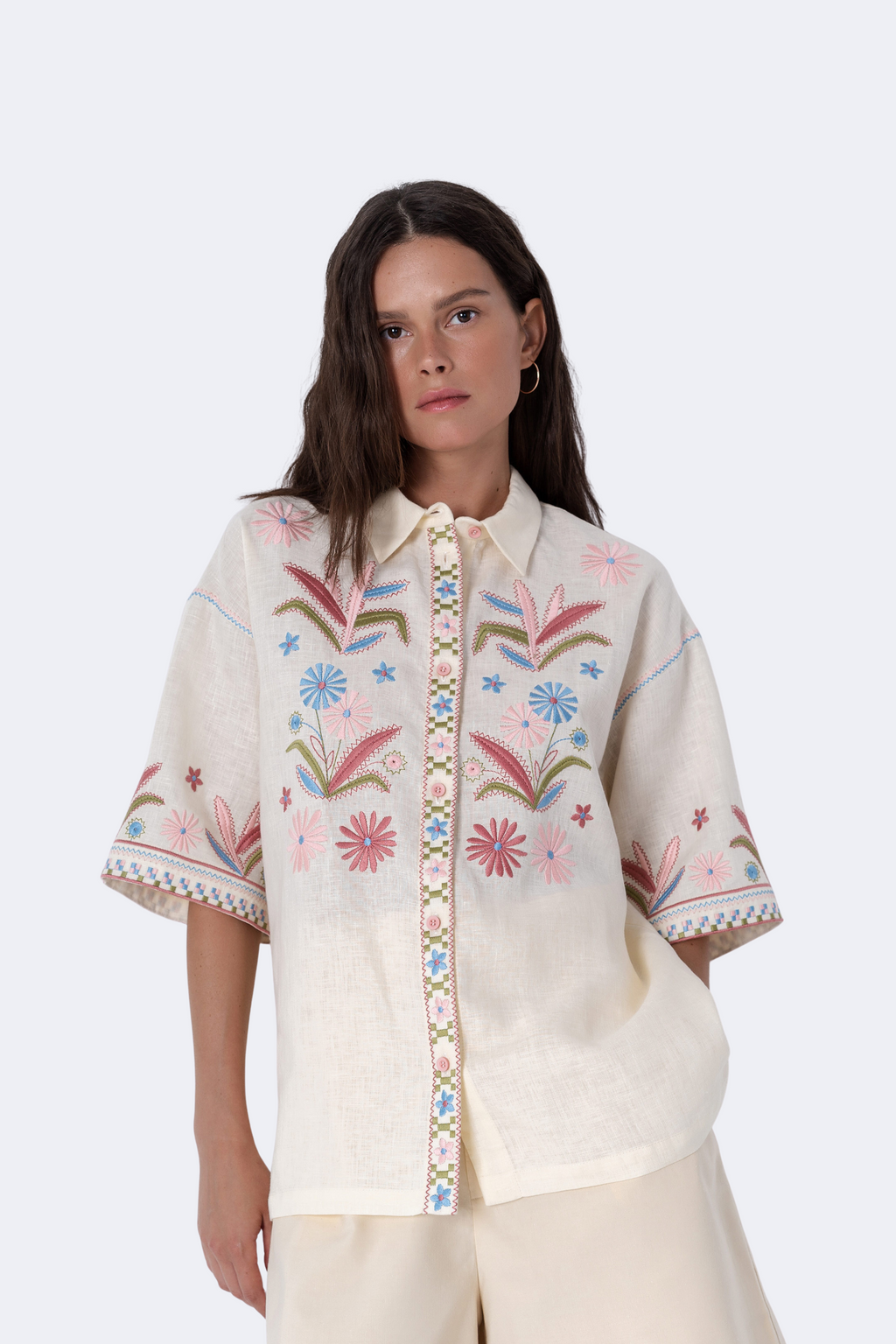 Woman wearing a cream-colored embroidered blouse with floral patterns on a white background