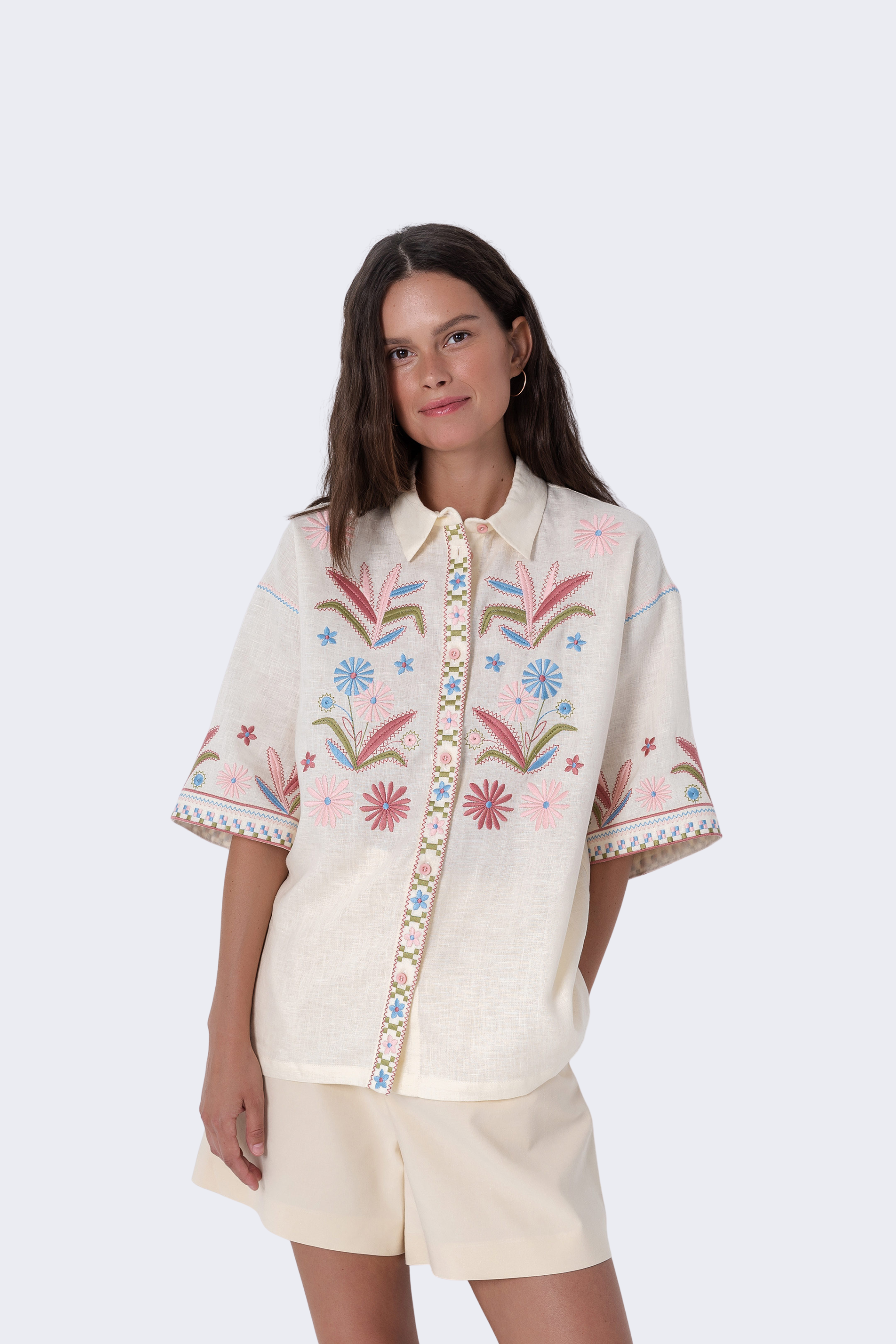 Woman wearing a cream-colored embroidered blouse with floral patterns on a white background