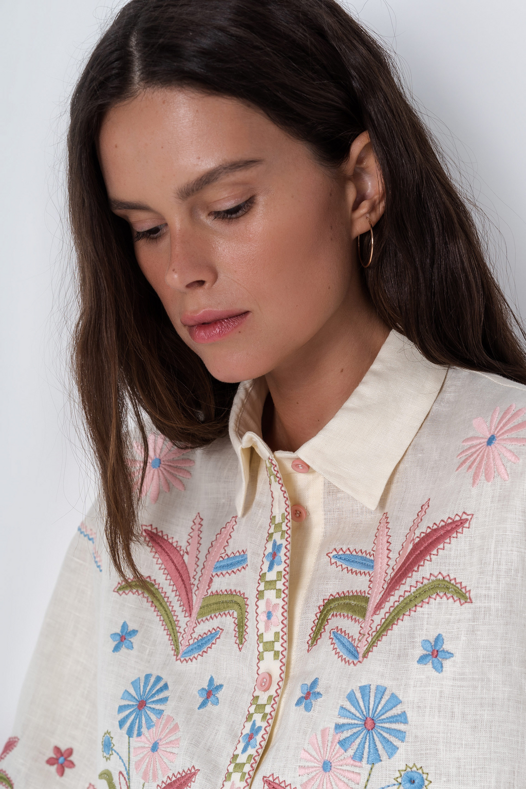 Woman wearing a cream-colored embroidered jacket with floral patterns on a white background