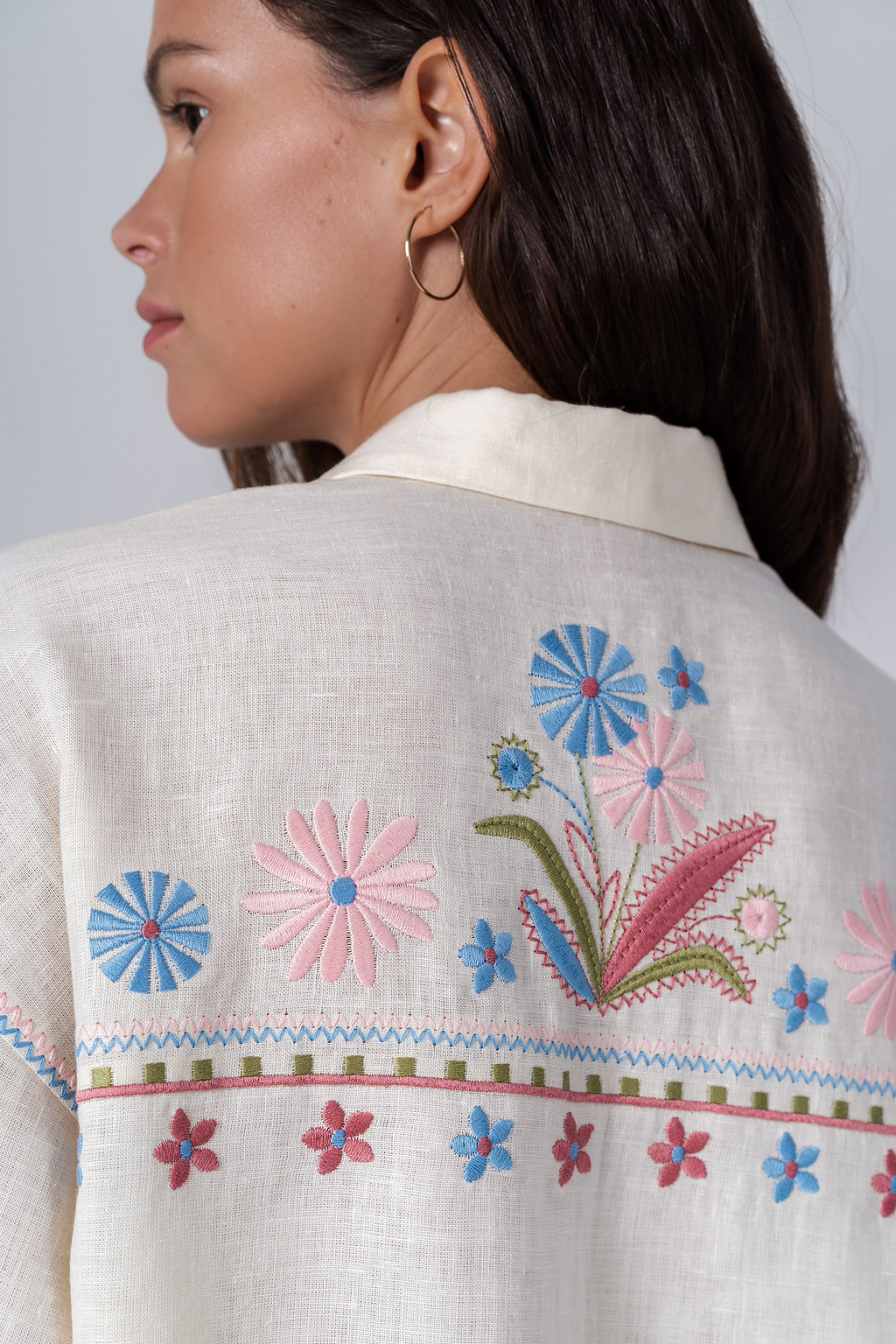 Close-up of a person wearing a white blouse with colorful floral embroidery on a plain background