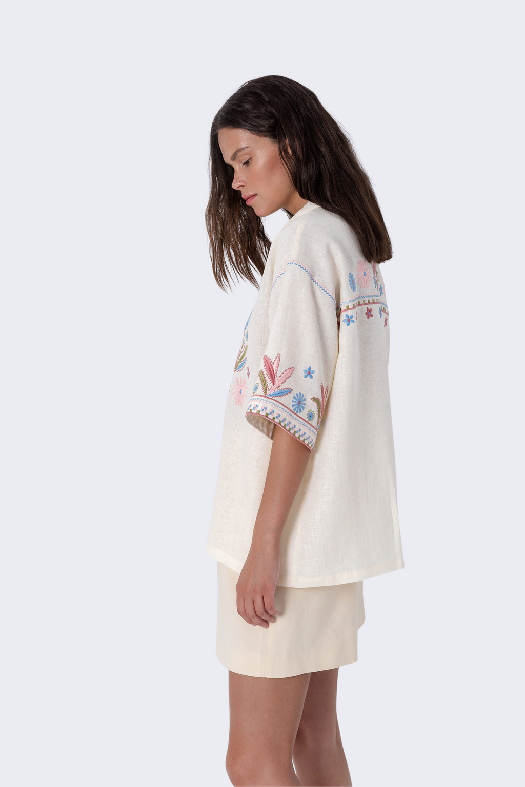 Woman wearing a cream-colored dress with floral embroidery on a white background